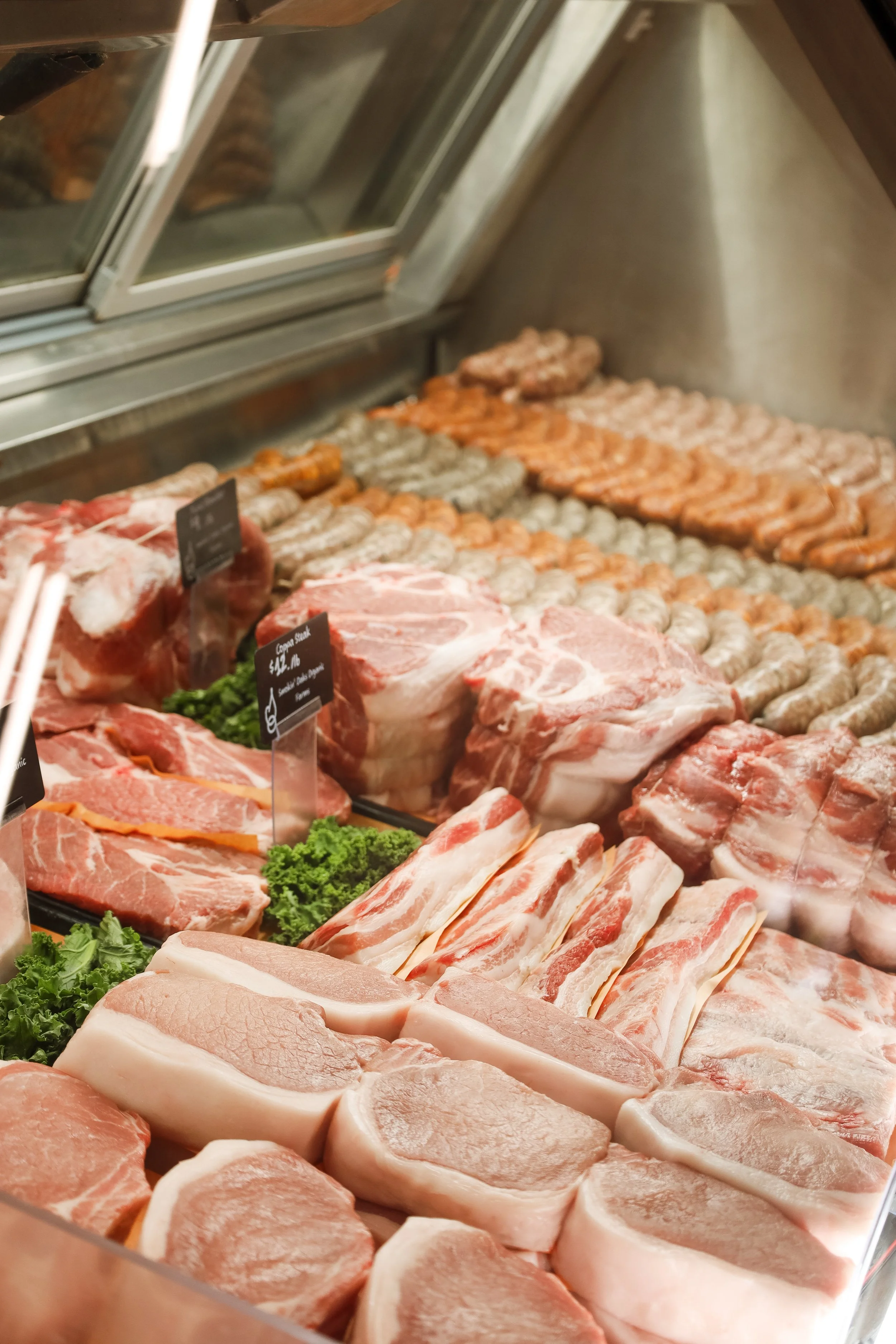 Display of assorted raw meats including pork chops, bacon, beef cuts, and sausages in a butcher shop or grocery store.