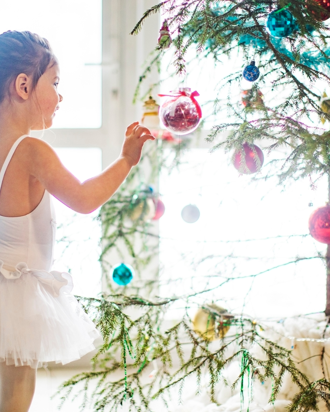 Little girl in tutu decorating her live Christmas tree with coloured balls