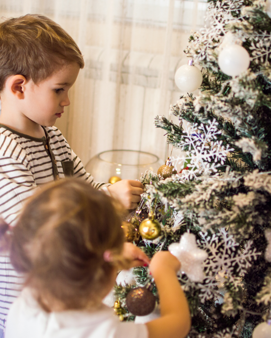 Young brother and sister decorating Christmas tree with snowflakes and gold ball ornaments
