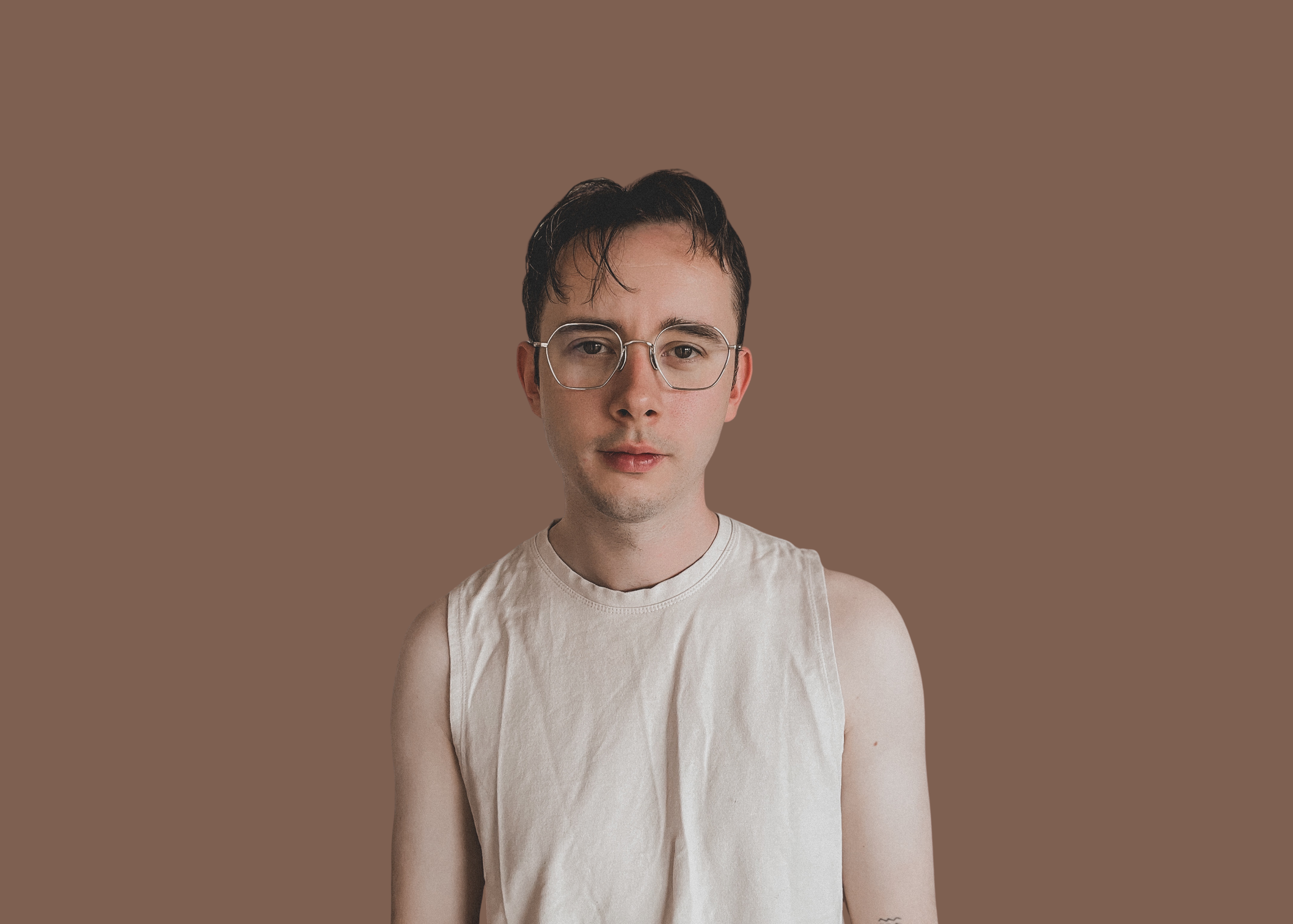A dark haired man who is a writing coach wearing glasses is on a brown background.