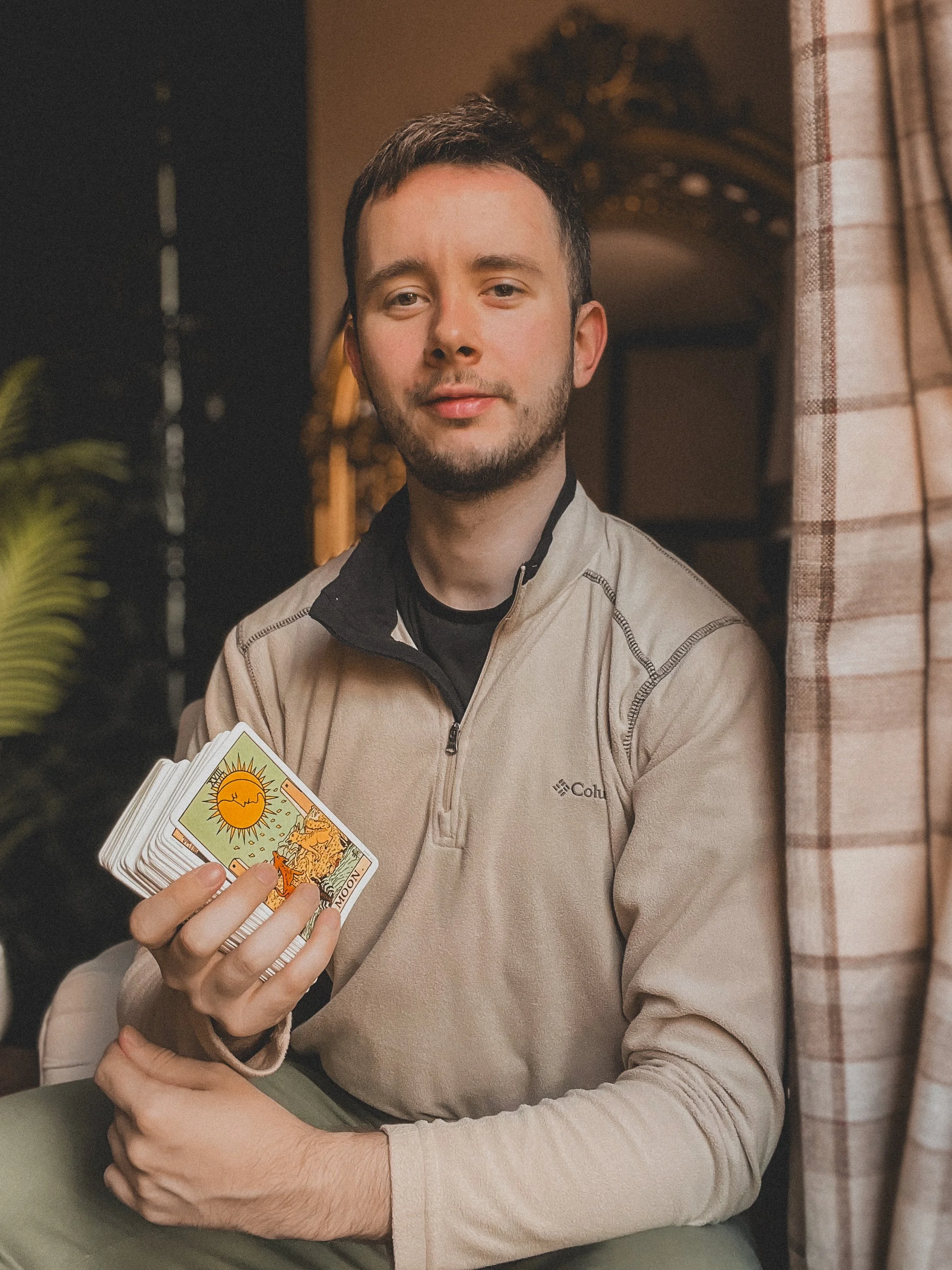 A dark haired man holds tarot cards