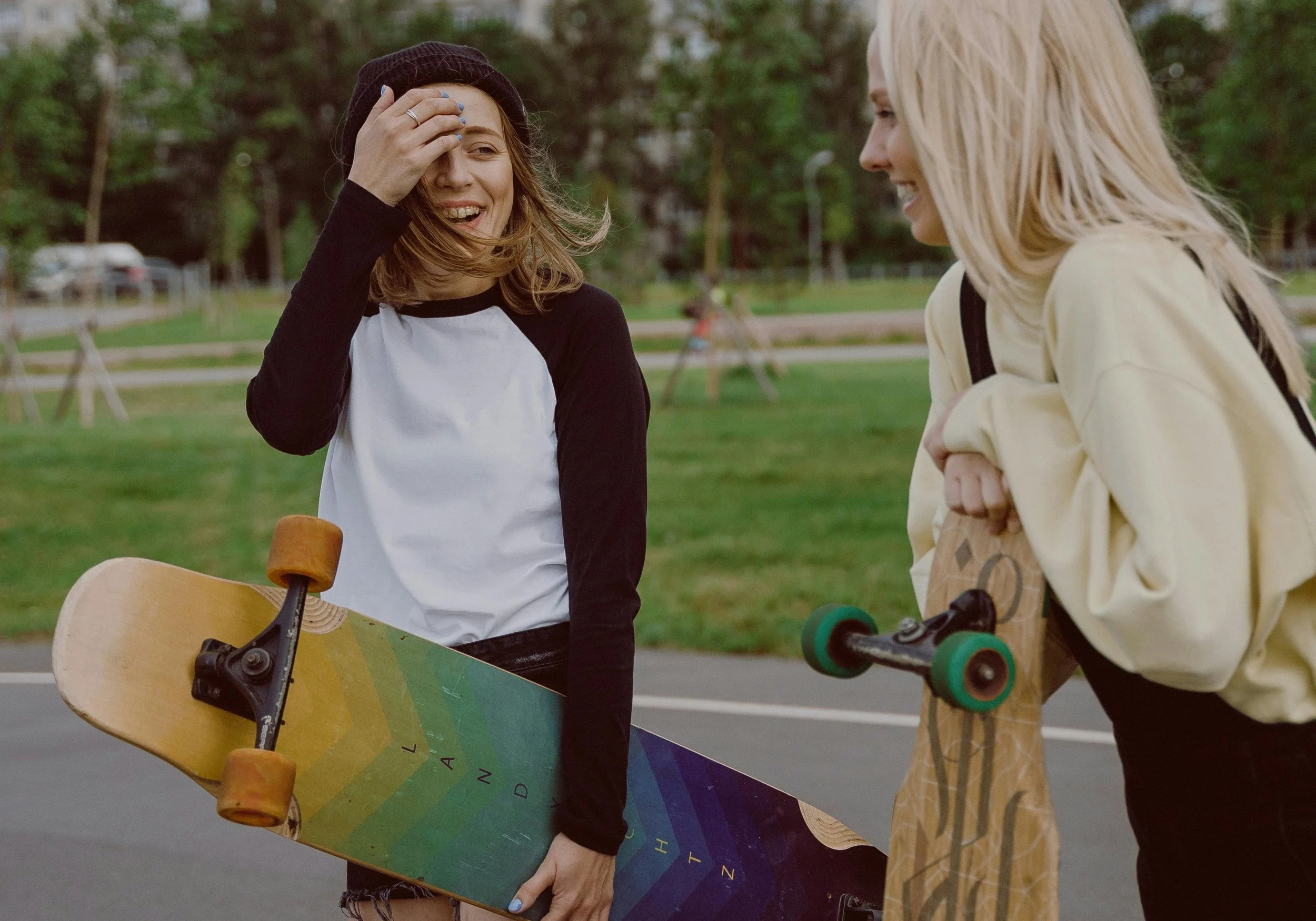 Teens laughing with each other in the park holding skateboards.