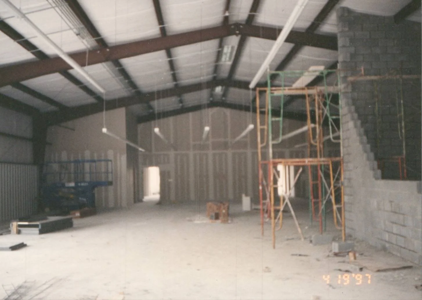 Interior of a large building under construction with scaffolding, unfinished walls, and construction materials on the floor.