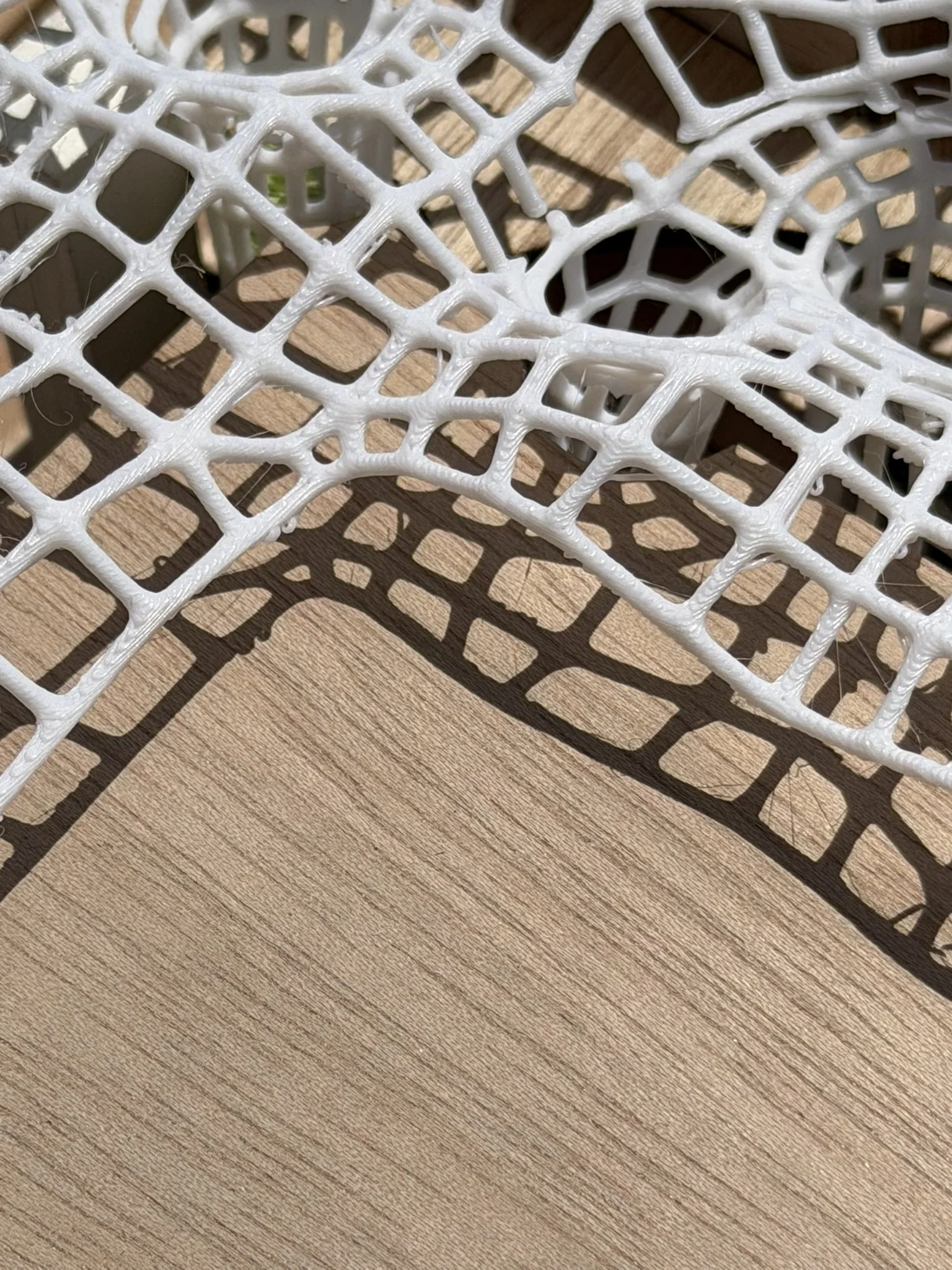 Close-up of a white tennis racket lying on a wooden surface, casting a shadow.