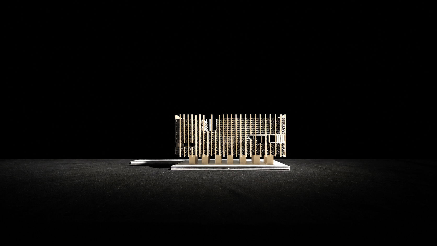A detailed architectural model of a modern building with a grid-like facade, placed on a base against a dark background.