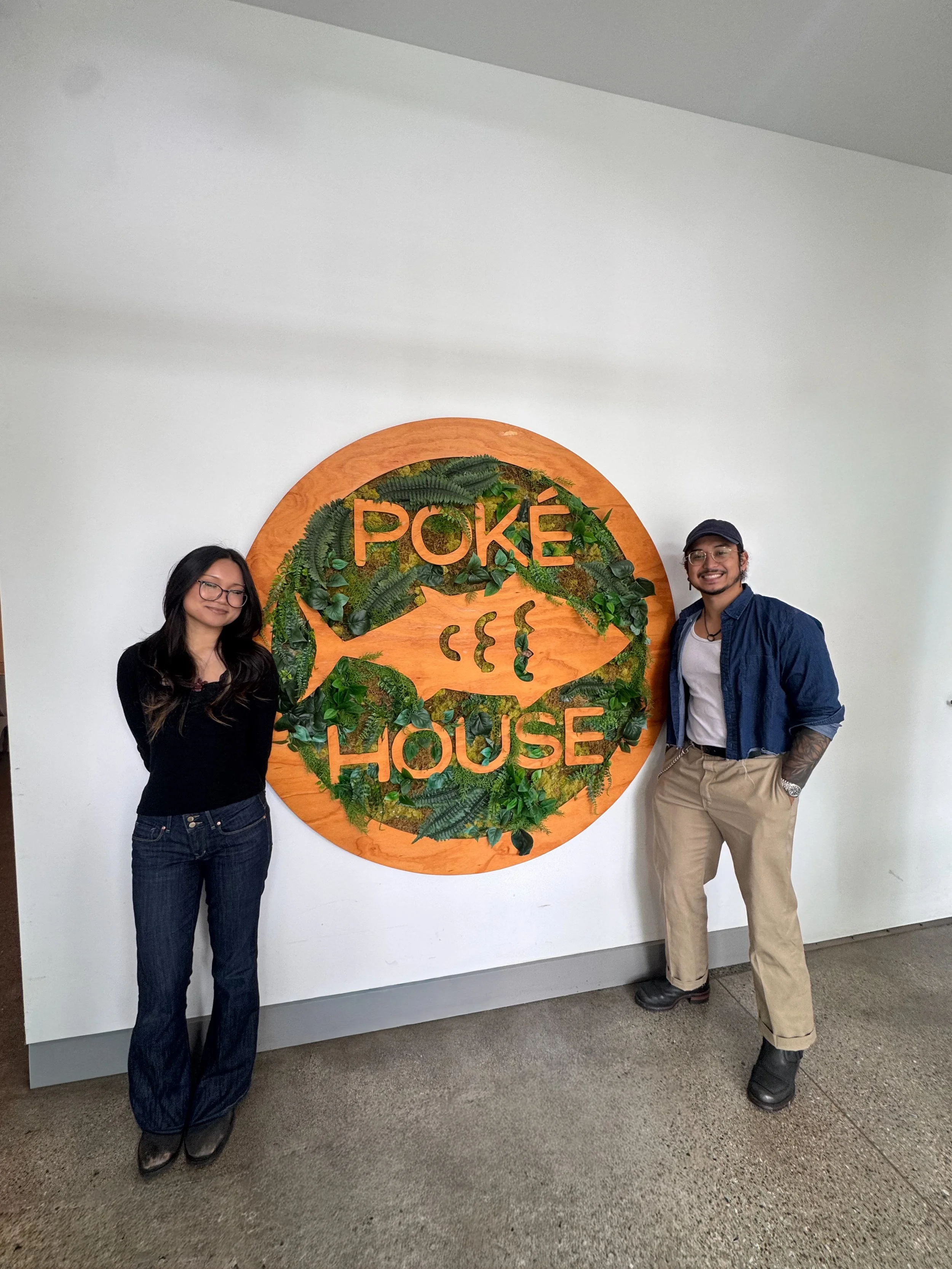 Poke House team members in front of Poke House logo art