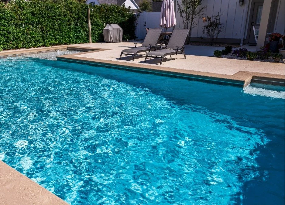 Residential backyard with a swimming pool, lounge chairs, and umbrellas, surrounded by a manicured garden.
