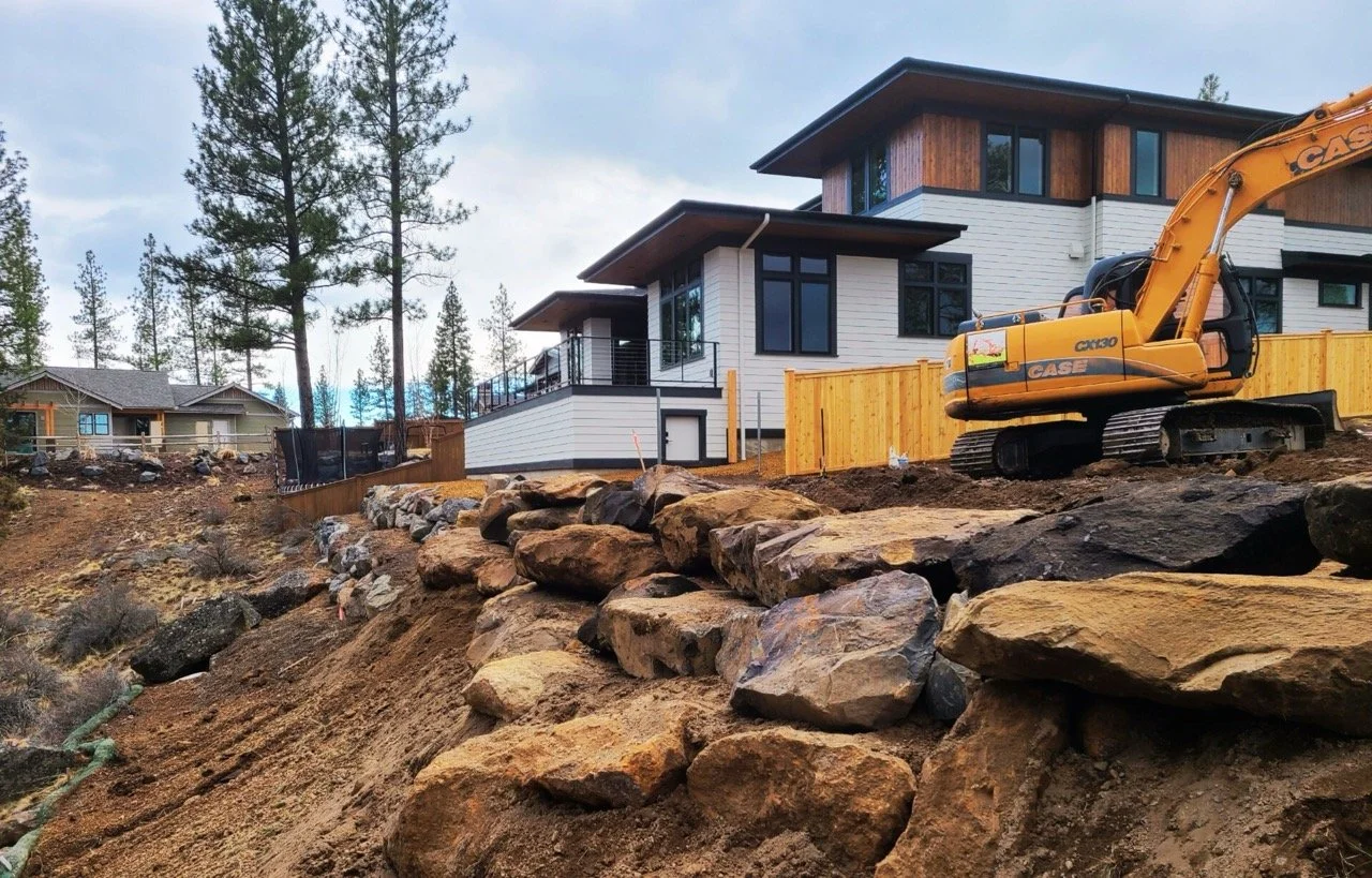 Excavator building a terraced retaining wall in a backyard of a residential excavation project in Bend Oregon.