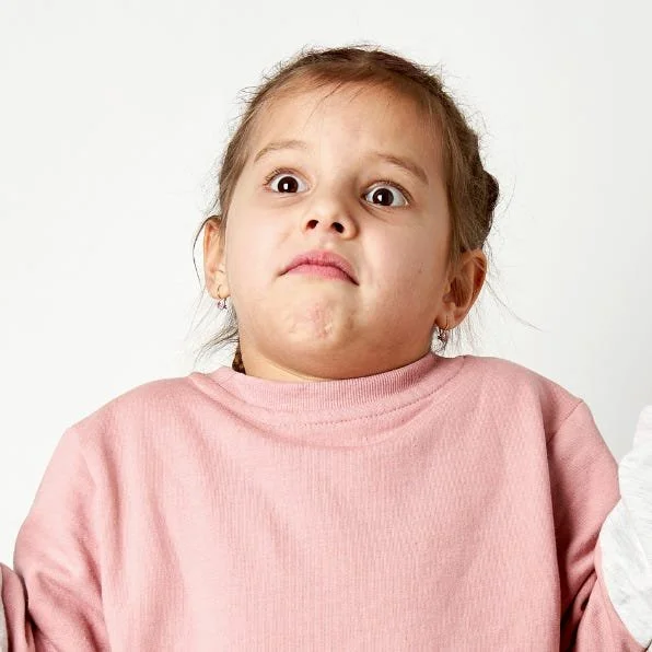 A young white girl wearing a pink sweater looking confused.