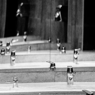 A black and white photo of a sink and a mirror. The reflection doesn't end.