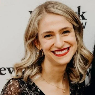 Smiling woman with blond hair wearing red lipstick and a black patterned top at an event.
