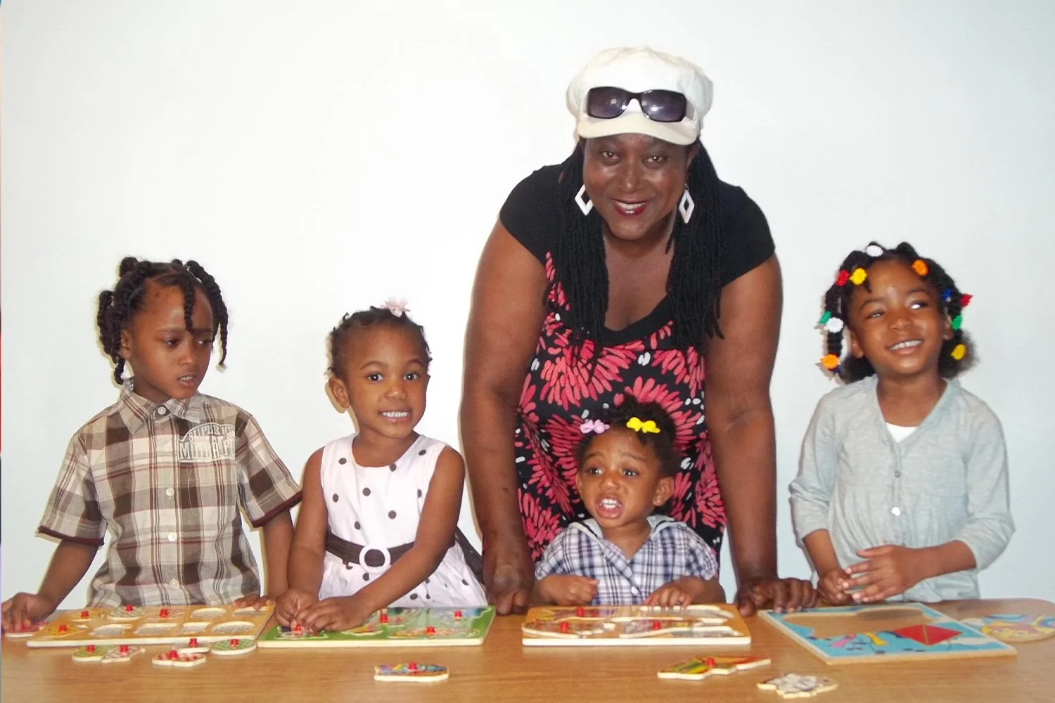  smiling black child care provider gathered alongside four children who are playing with puzzles 