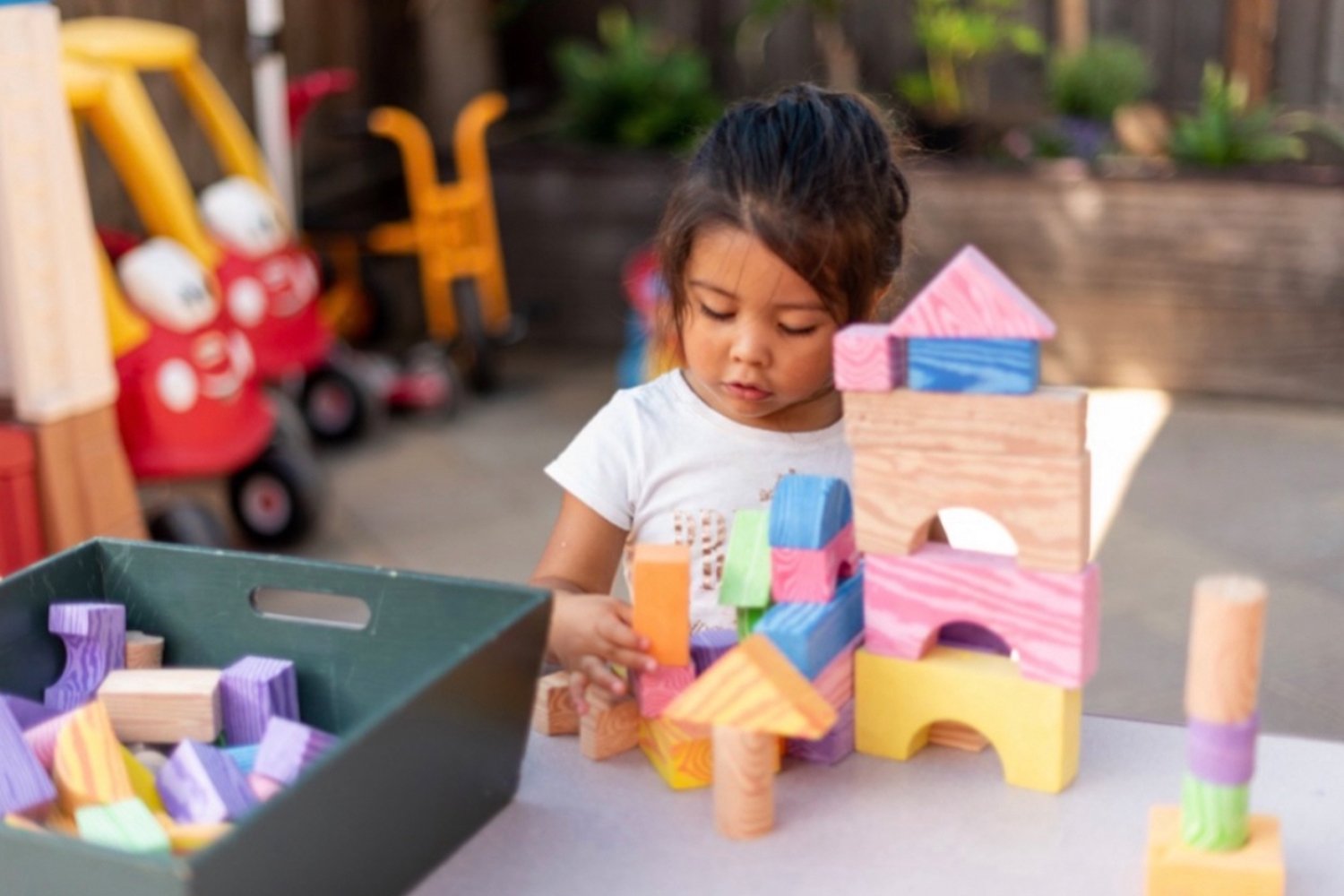  young latina girl intently focused on playing with colorful wooden blocks at a play table outside 
