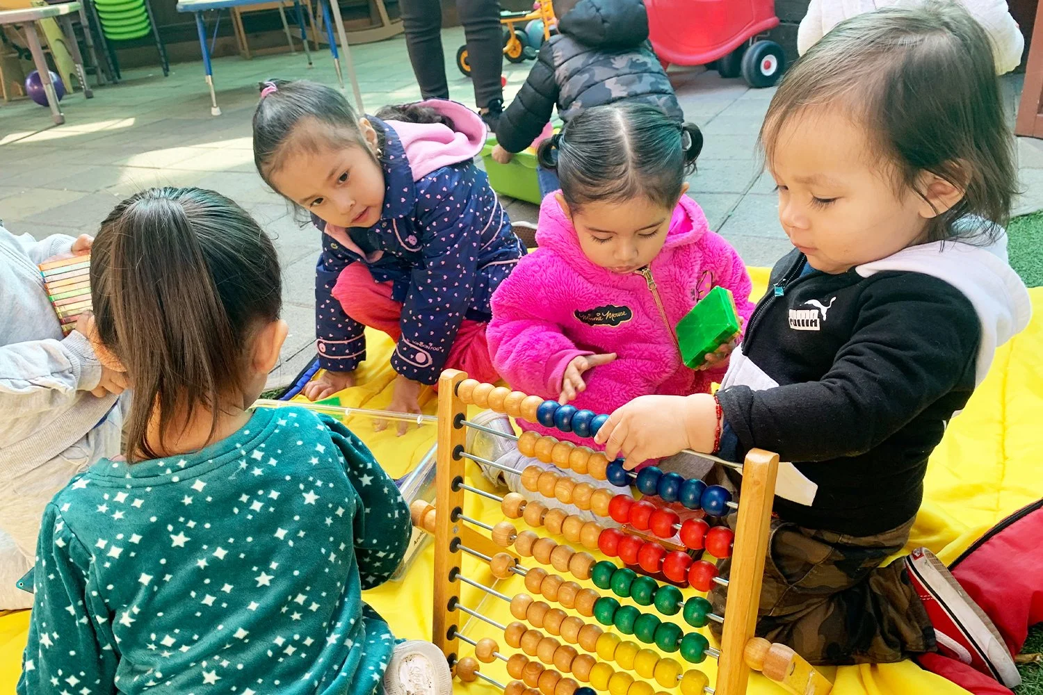  small group of diverse children engaged in play with various colorful toys including an abacus while seated on a blanket 