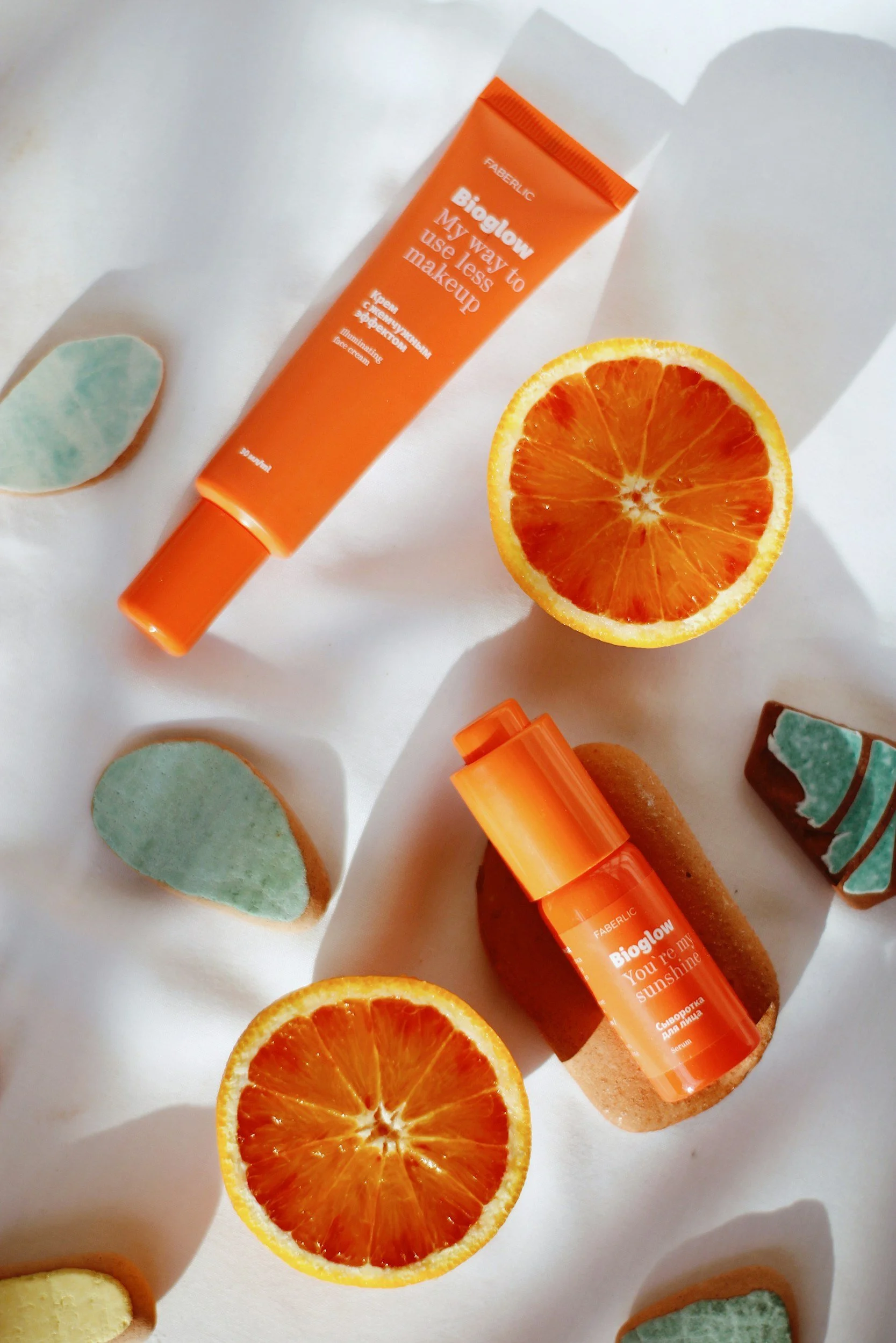 Skincare products with bright orange packaging labeled 'Bioglow', surrounded by orange slices and decorative stones.
