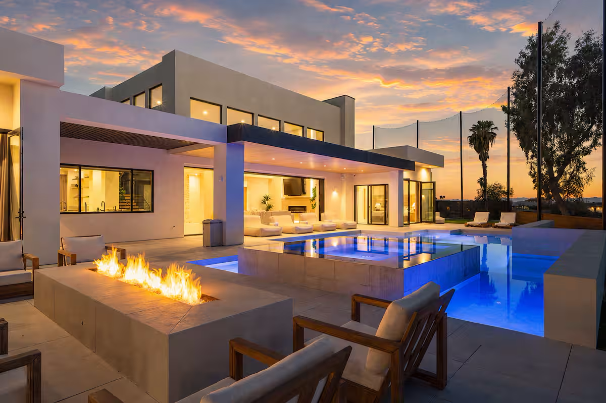 Backyard of Aura house at night with illuminated pool and spa, and firepit in the foreground
