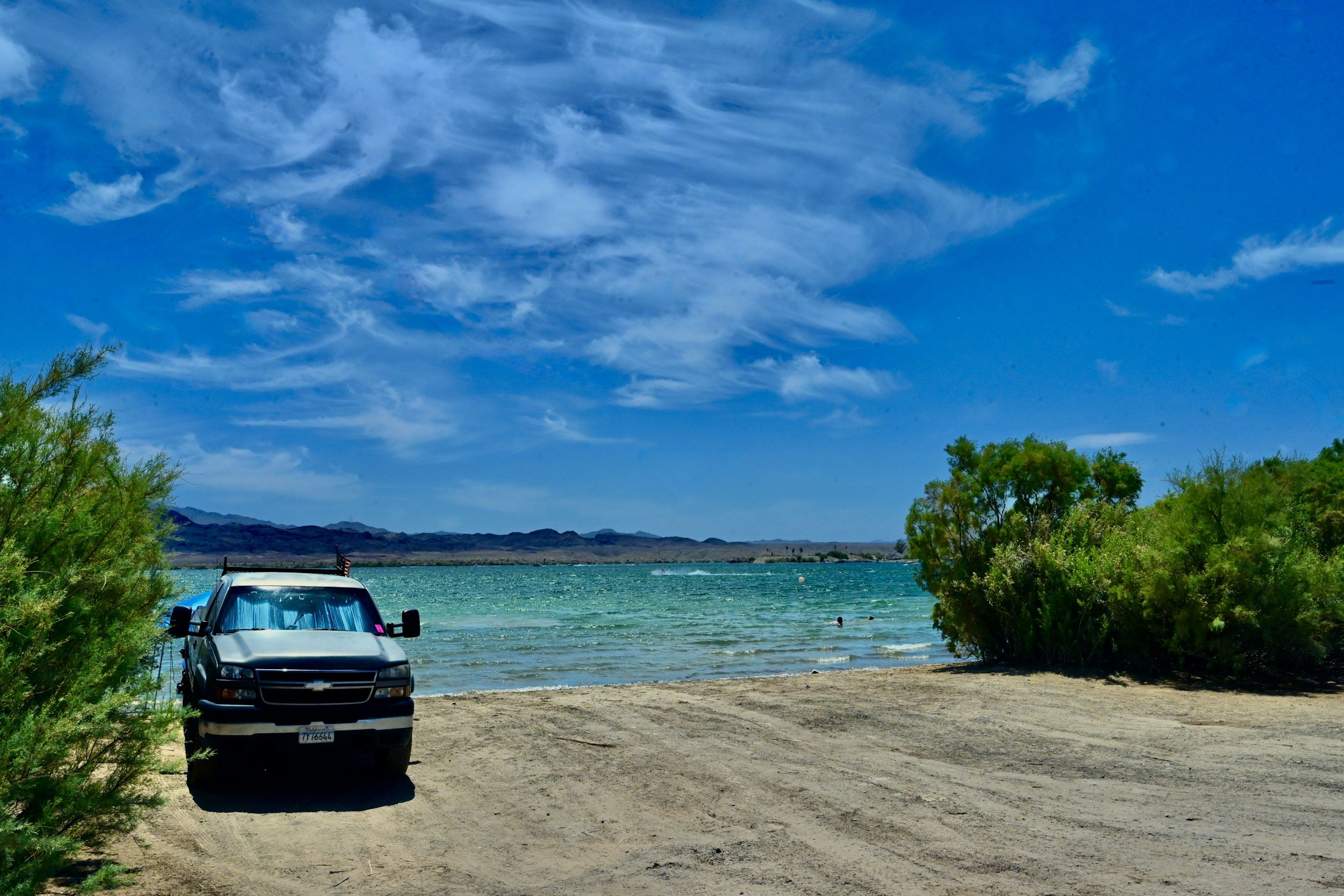 Shoreline of Lake Havasu with sand, bushes and a pickup truck backed up to water's edge