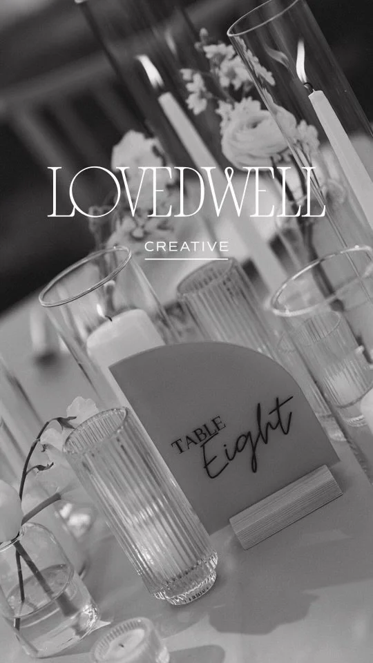Table decoration with candles, floral arrangement, and a sign labeled 'Table Eight' on a white tablecloth, featuring the text 'LOVEDWELL CREATIVE' in the foreground.