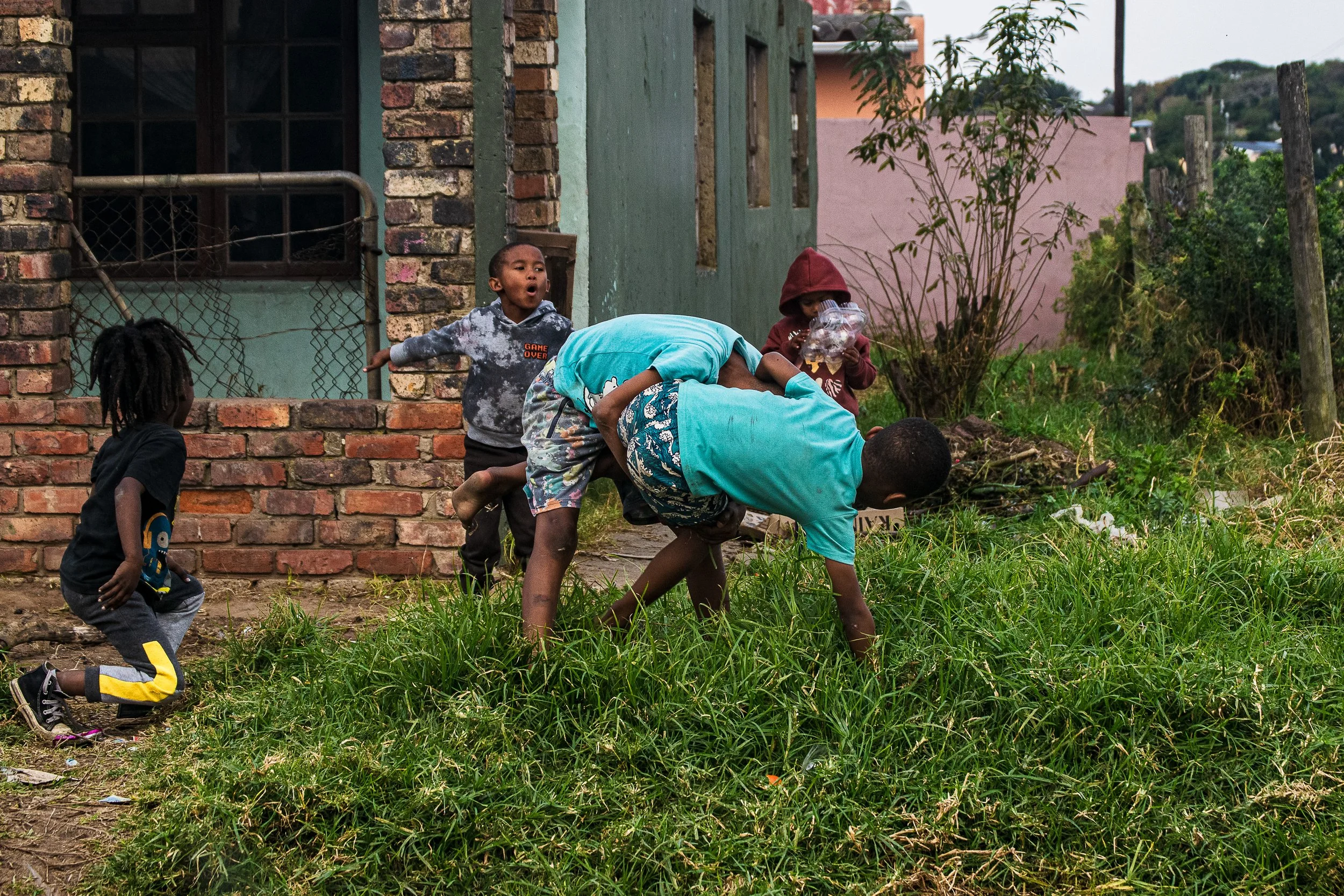 A group of young boys watching as twin brother fight outside their homes