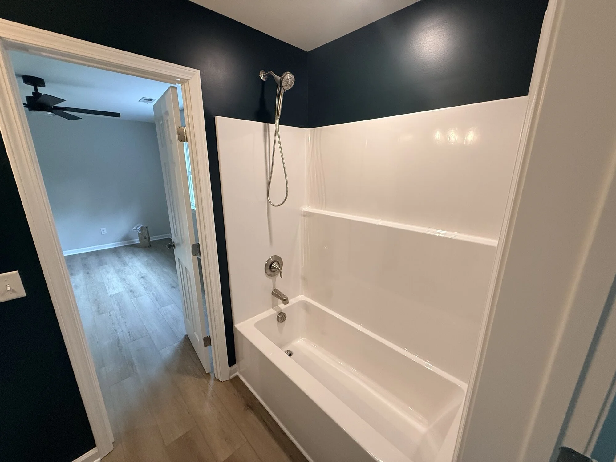 After — hall bath with new tub and surround, dramatic navy walls, and updated fixtures