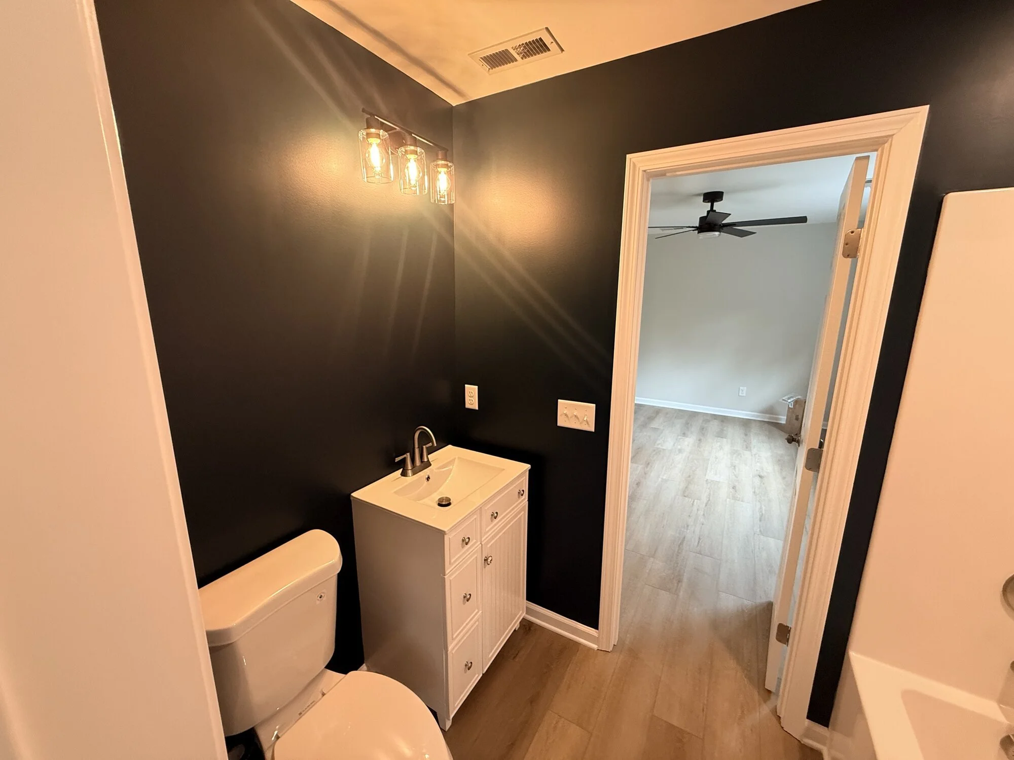 After — moody hall bath finished with new vanity, sconces, and wood-look floors