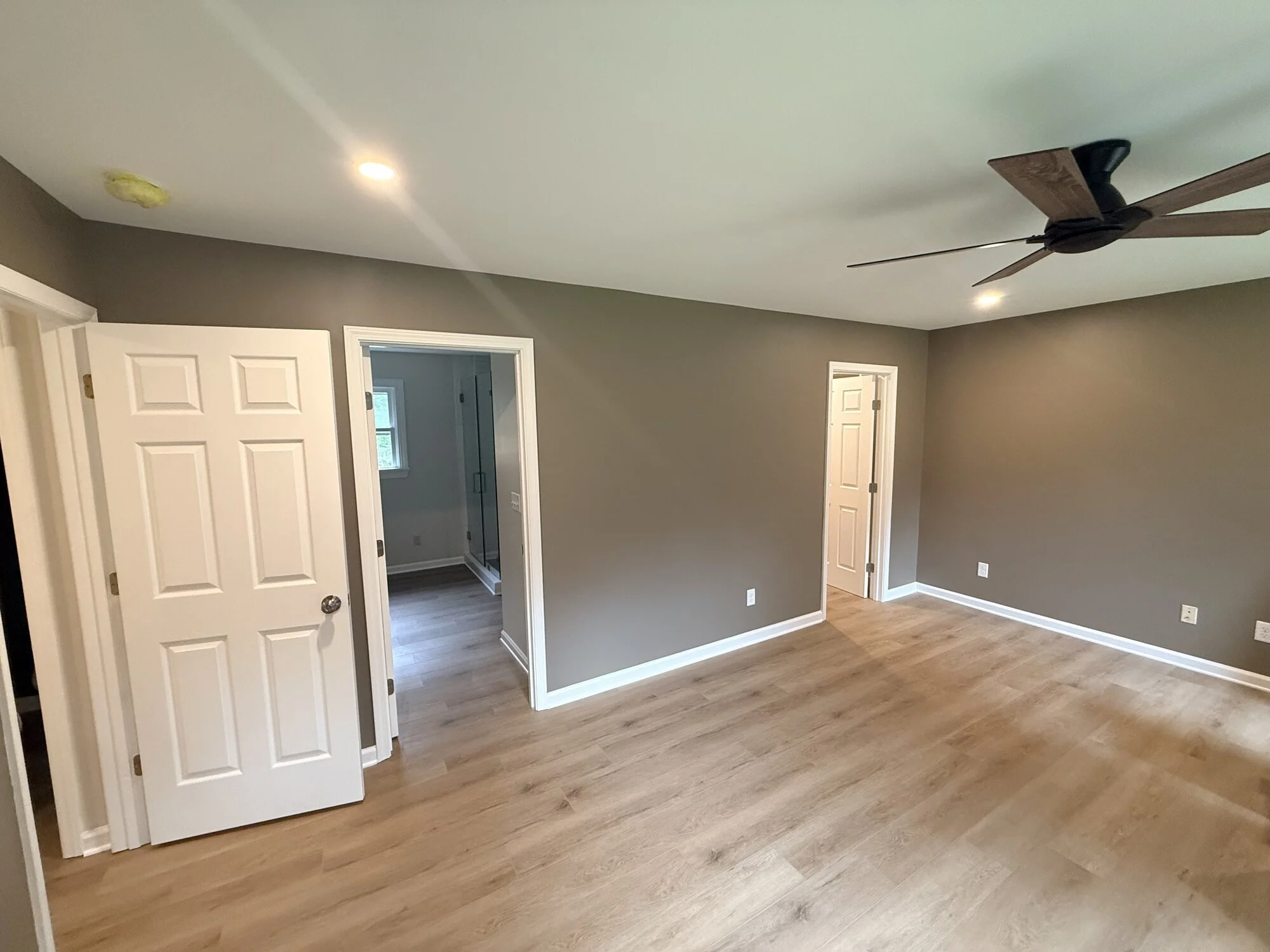 After — Primary bedroom refinished with warm gray walls, new flooring, and modern fan along with new closet and bathroom entrances