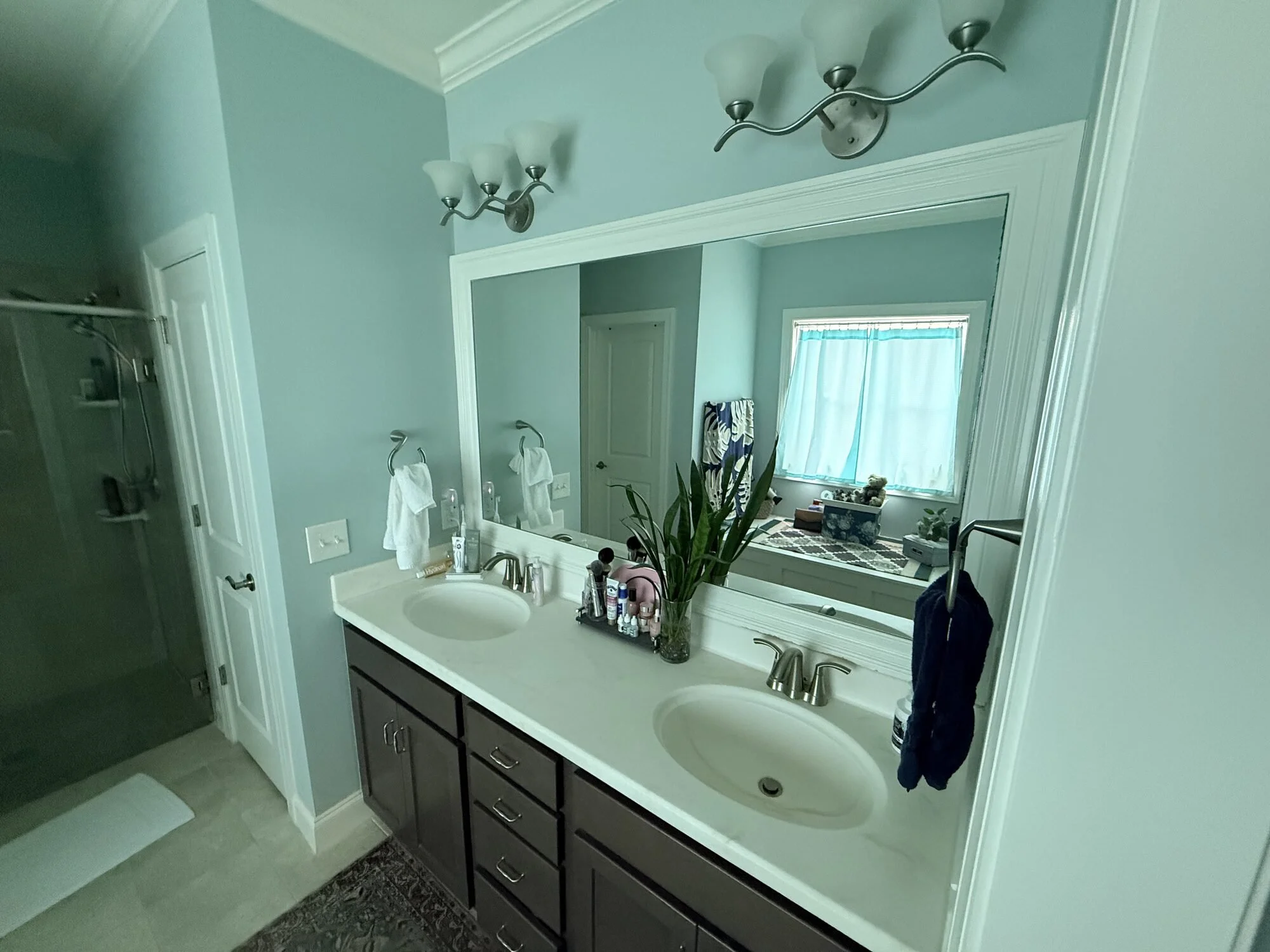 Before — double vanity with dated strip lighting and plate glass mirror