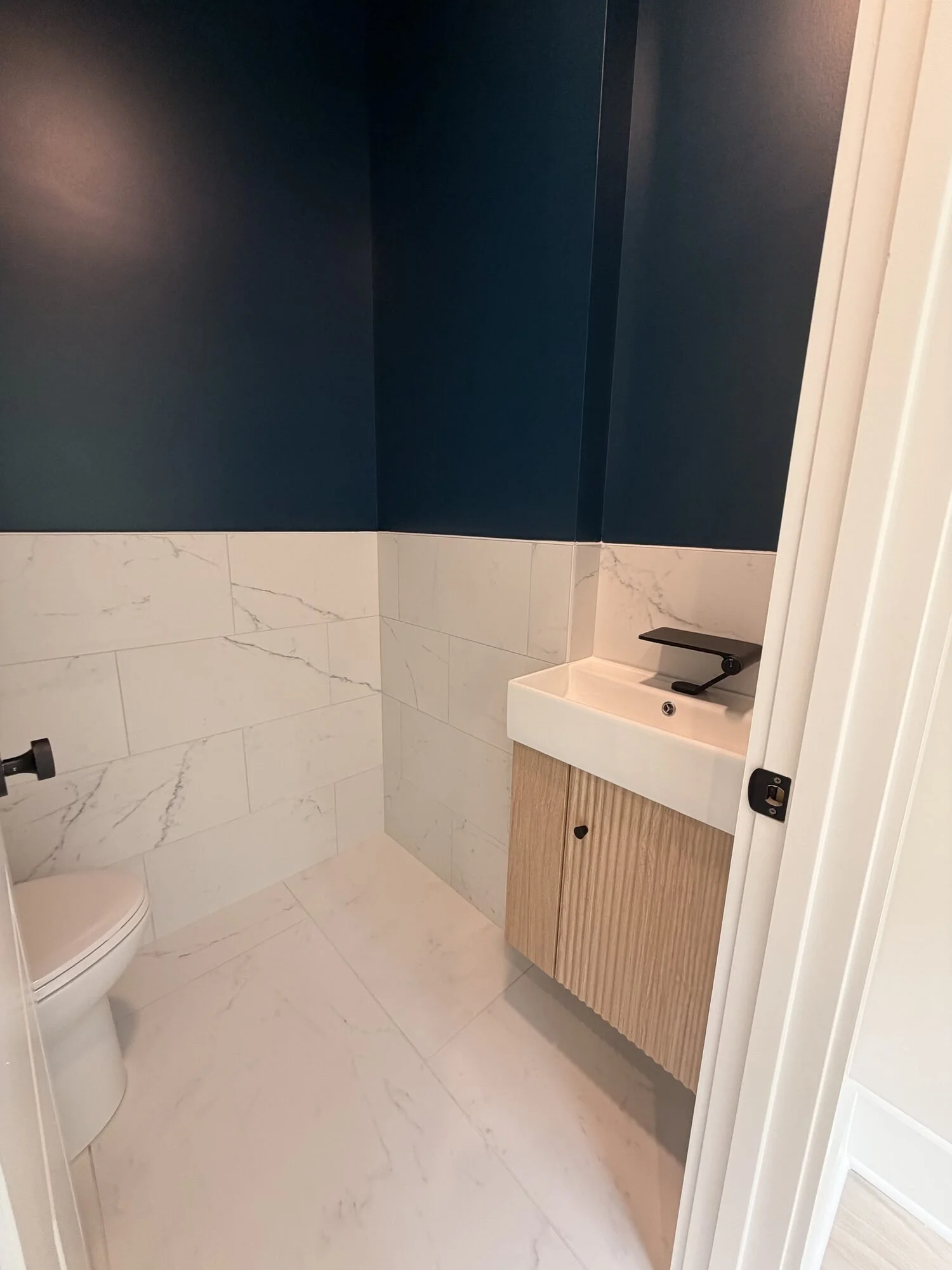 After — powder bath with navy walls and fluted natural wood floating vanity