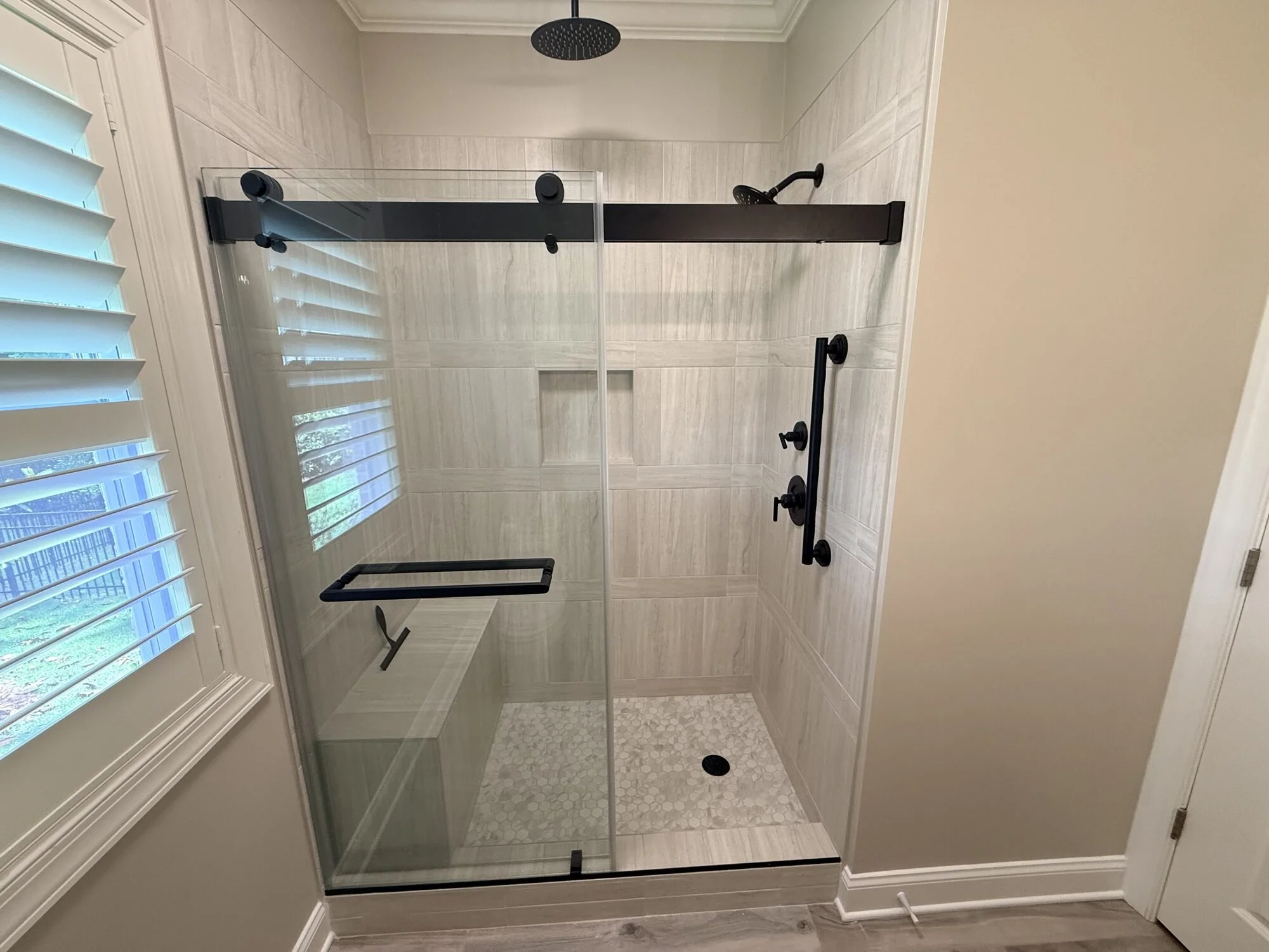 After — tub converted to a walk-in tile shower with black sliding glass door, grab bars, and rain head