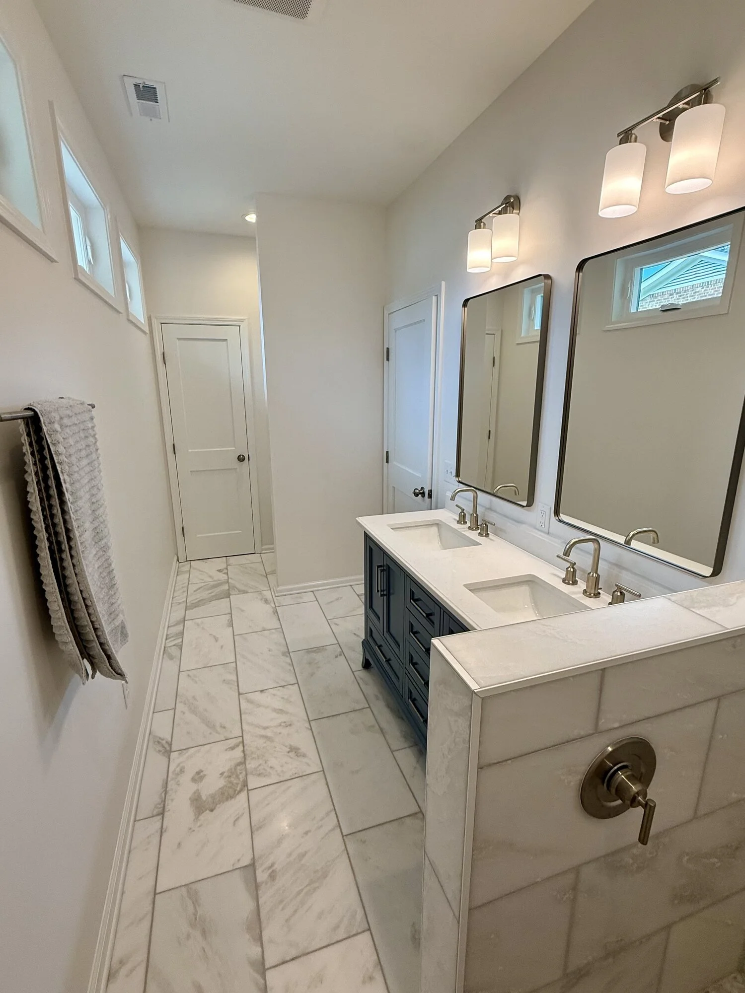 After — dual mirrors and widespread faucets, daylight pouring in from the transom windows above