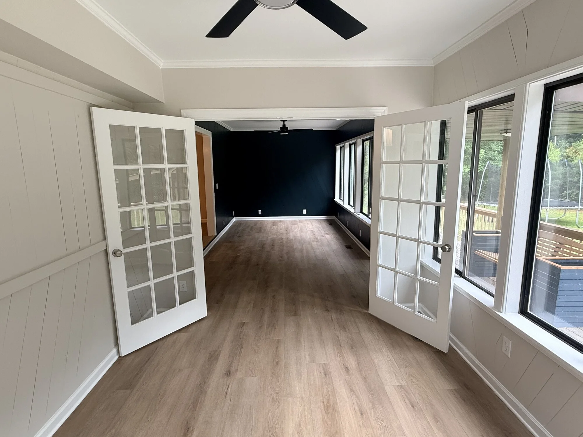After — sunroom brightened with French doors, moody accent wall, and new flooring