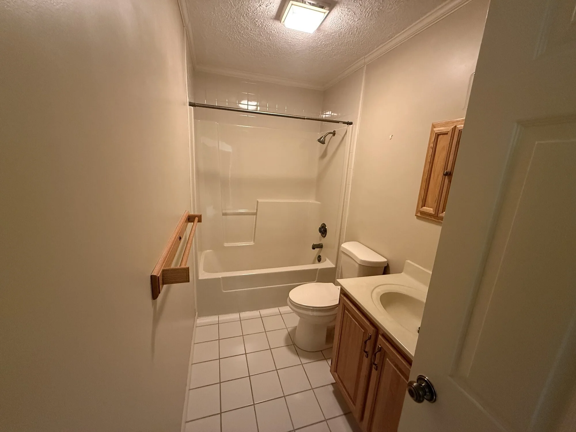Before — hall bath with dated tub surround, vanity, and tile floor