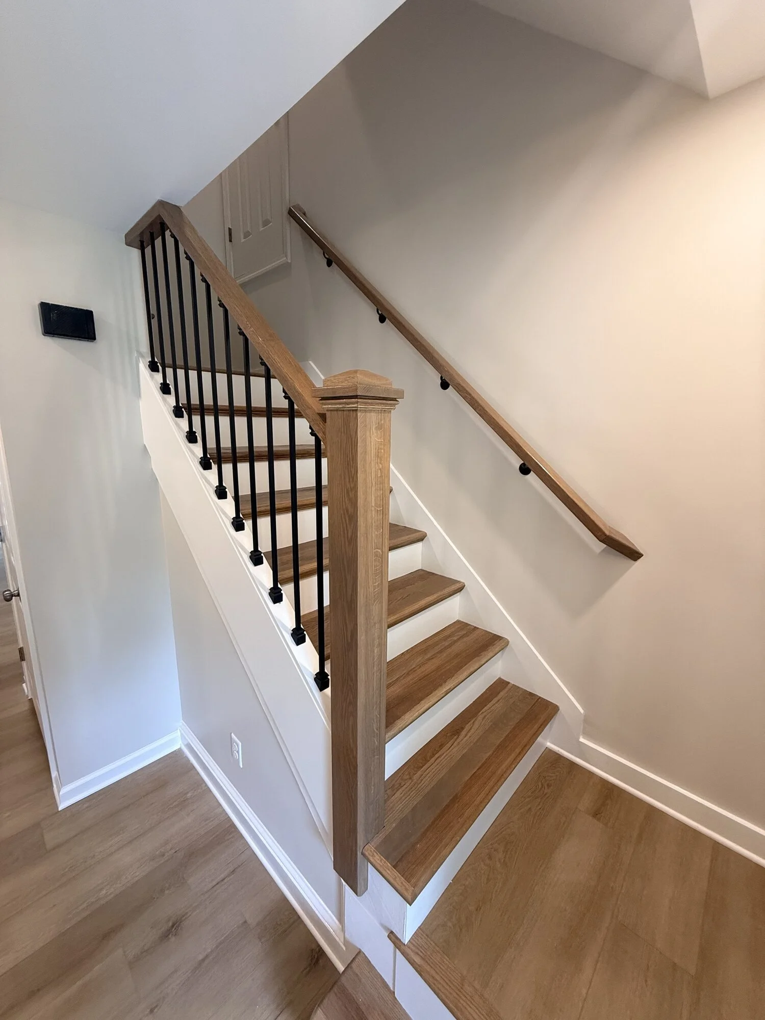 After — rebuilt staircase with wood treads, black metal balusters, and crisp white trim