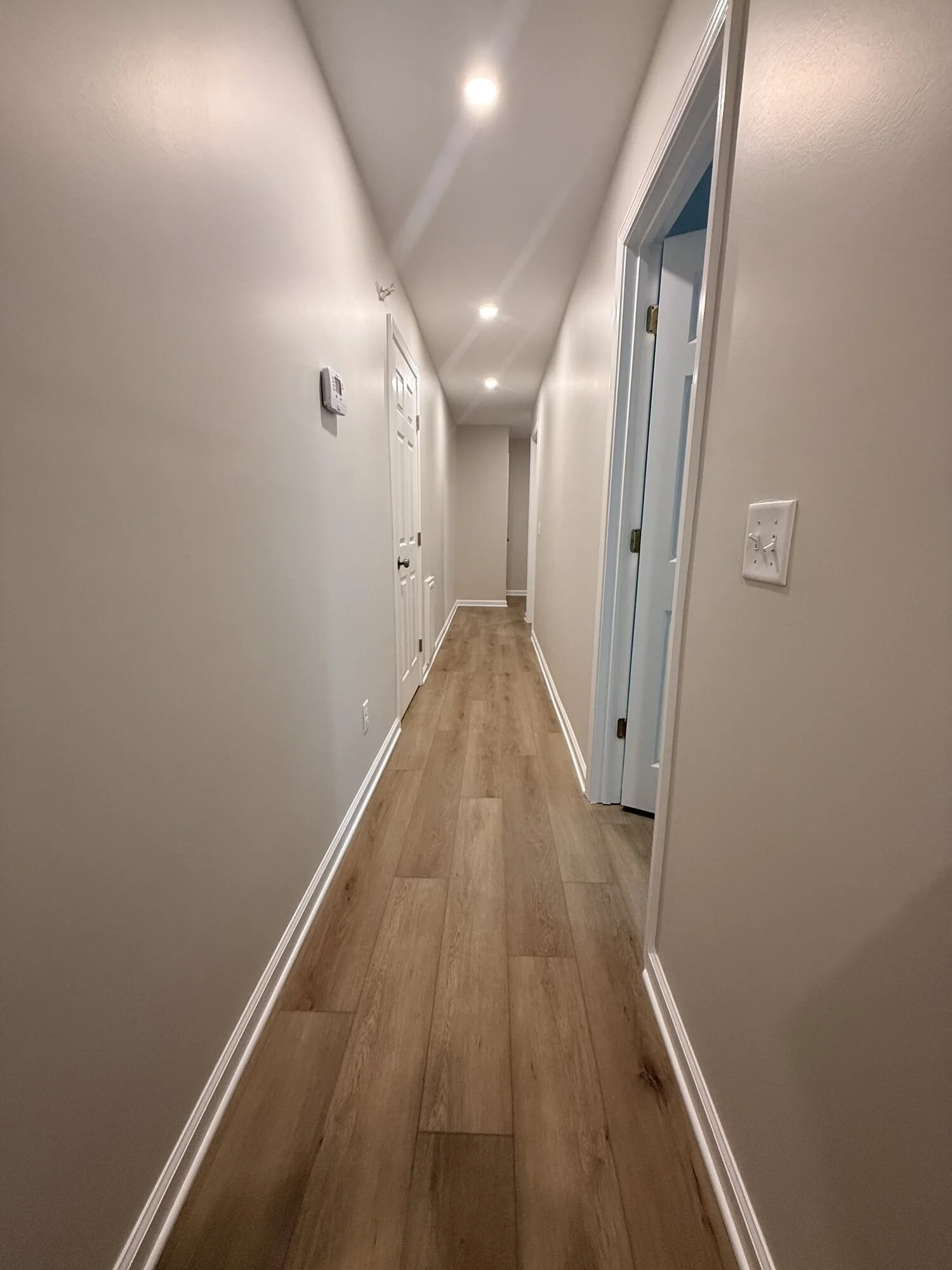 After — the same hallway brightened with new flooring, doors, trim, and recessed lighting