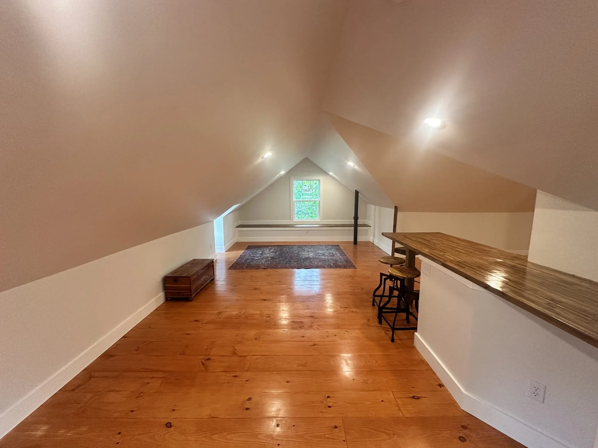 After — the long view: bar counter riding the knee wall, rustic pine floors glowing
