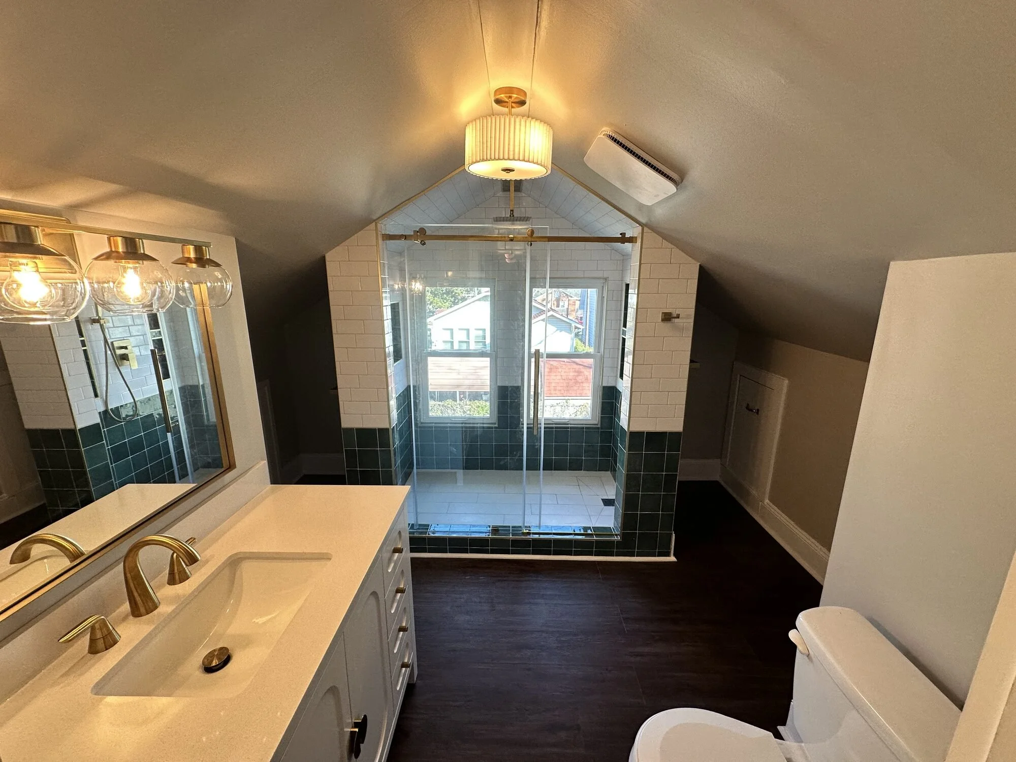 After — the full attic bath under the gable, with pleated drum light and brass finishes throughout