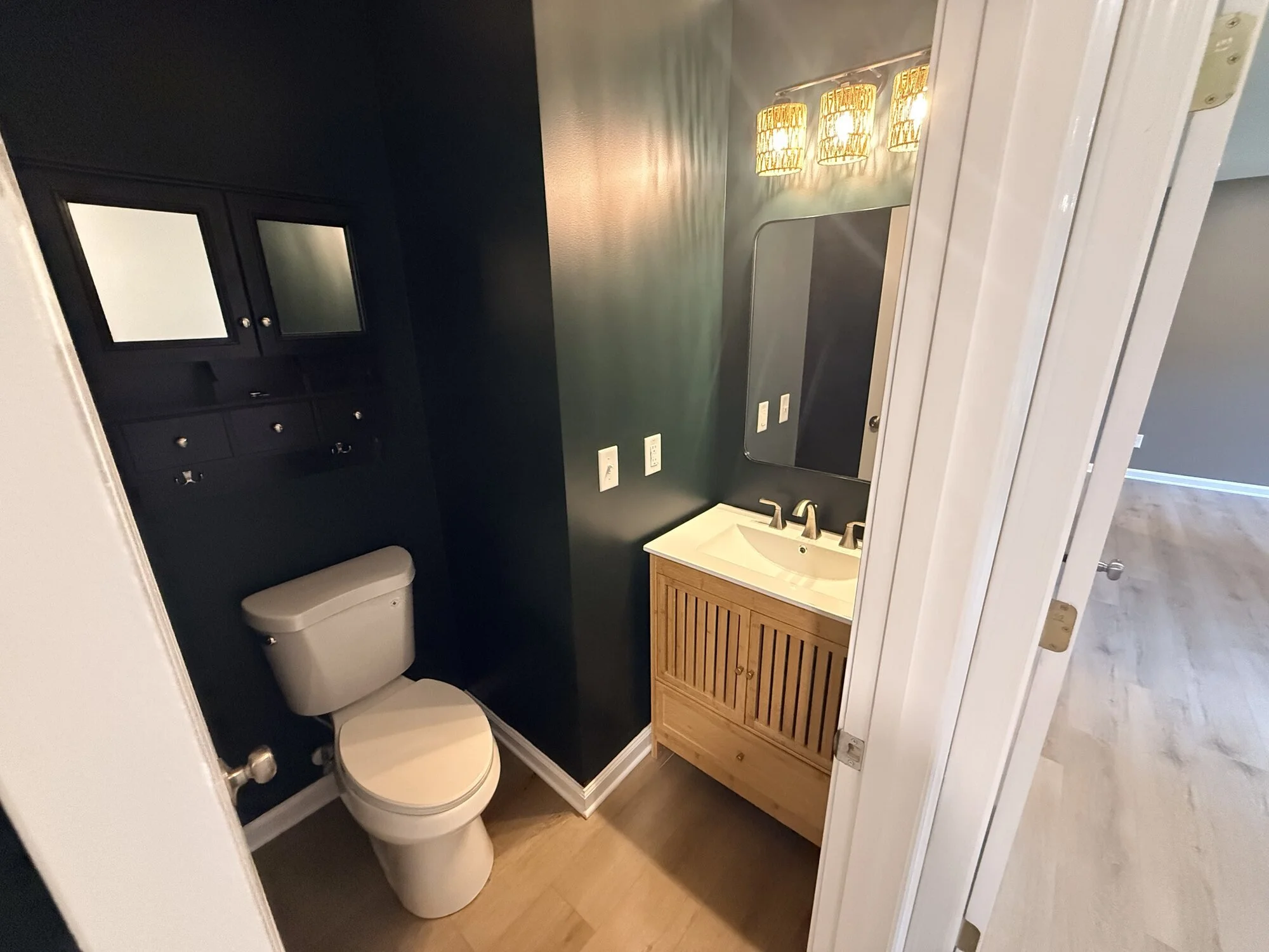 After — redesigned powder room with bold wall paint, floating wood vanity, and glam lighting