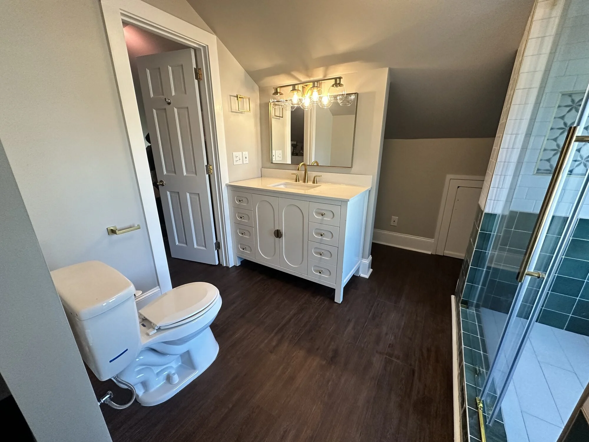 After — white vanity with quartz top, brass widespread faucet, and framed mirror under the eave