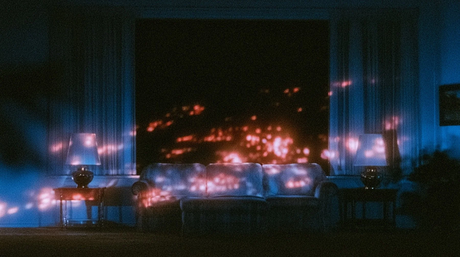 An empty living room at night, a sofa lit only by the flicker of a television that sits out of frame.