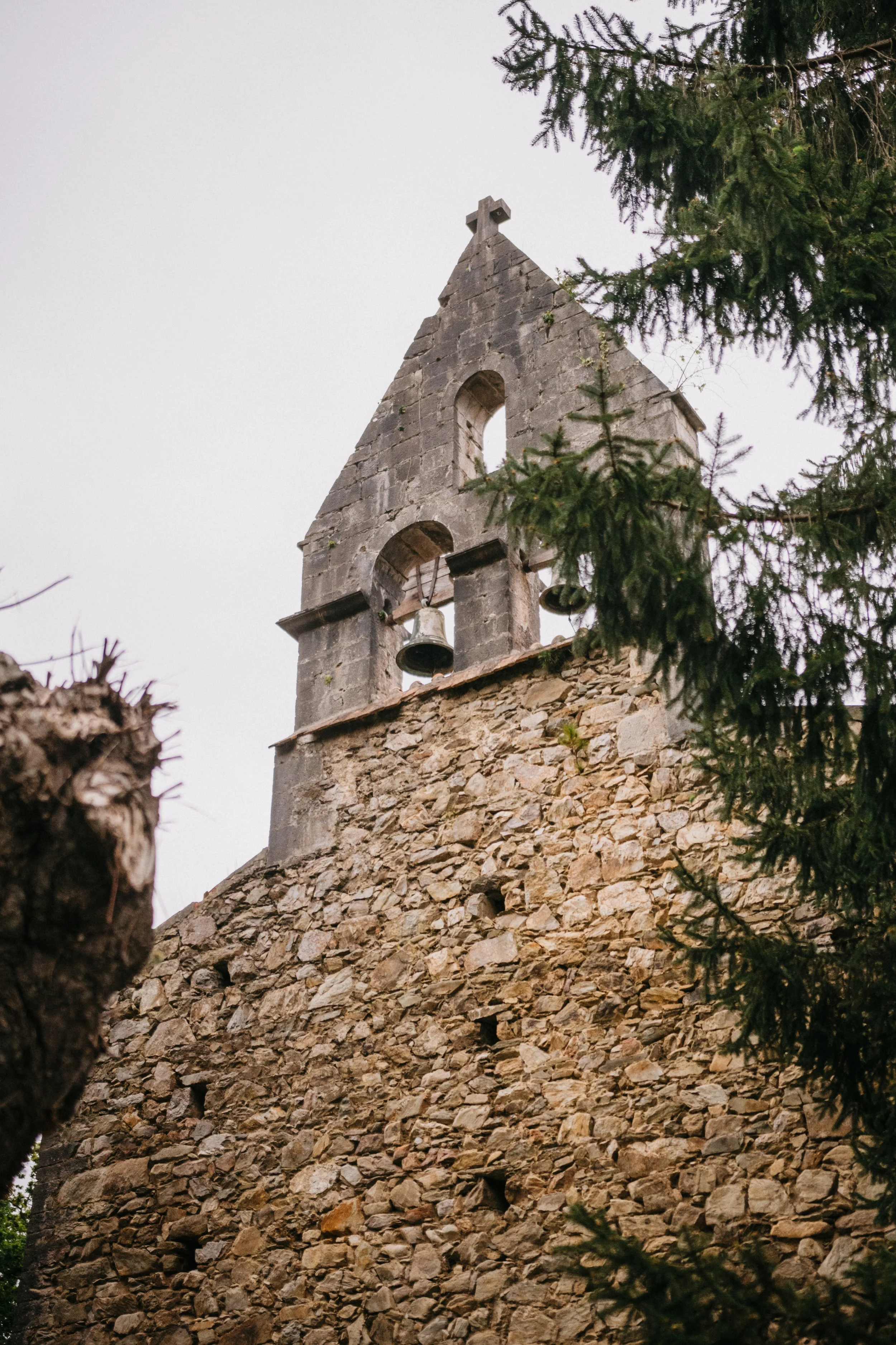 Campanario de una iglesia antigua de piedra, con árboles a los lados.