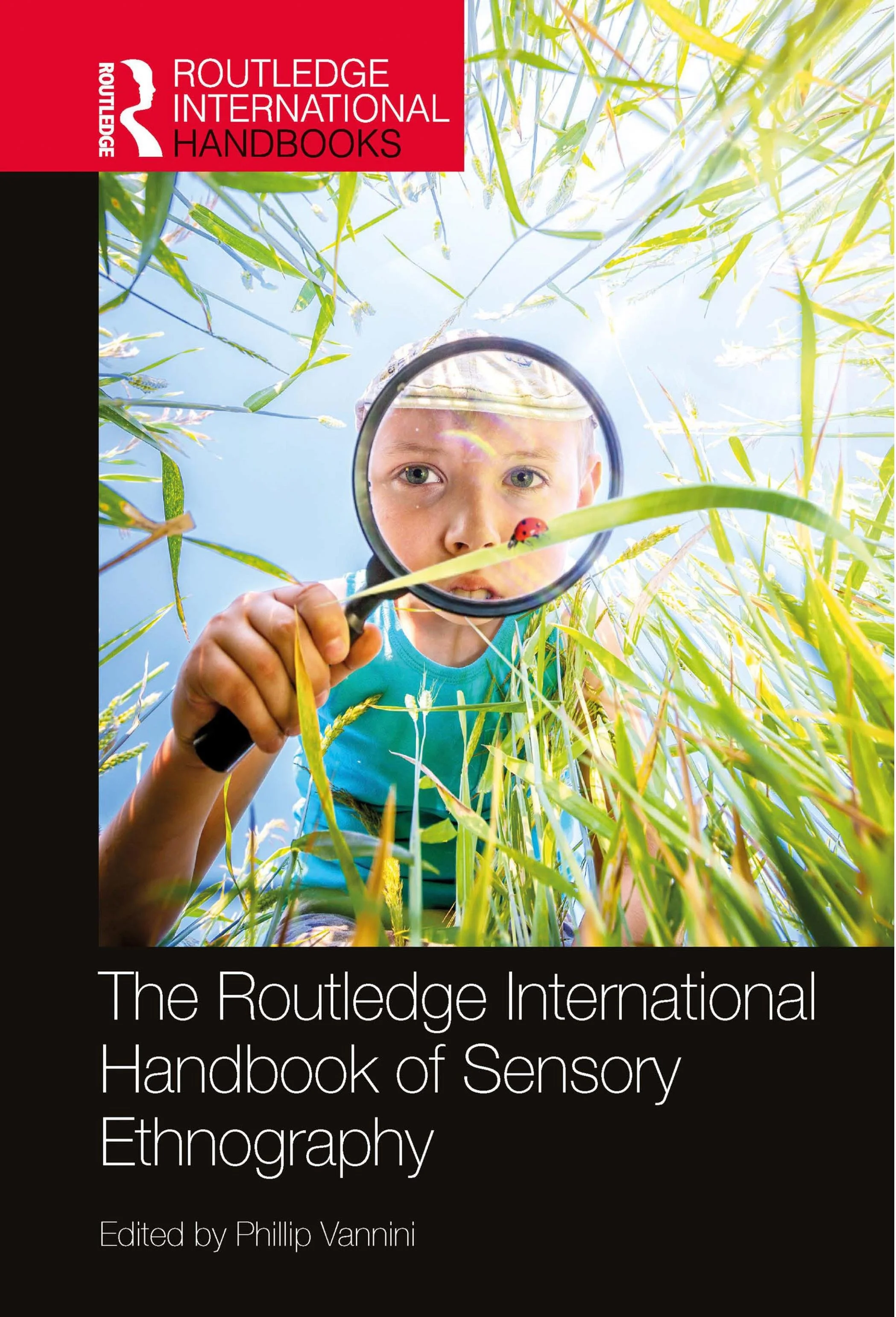 A book cover titled "The Routledge International Handbook of Sensory Ethnography," edited by Phillip Vannini. The cover features a child examining a ladybug on a blade of grass with a magnifying glass.