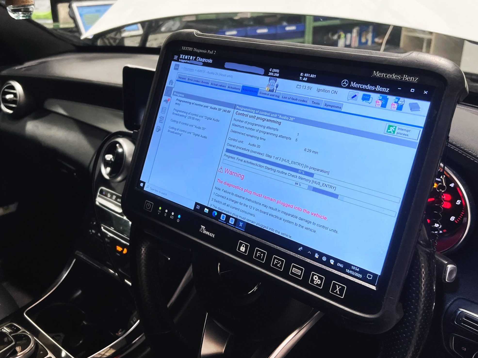 Inside a Mercedes-Benz vehicle, a diagnostic tablet displays vehicle diagnostics and control programming information.