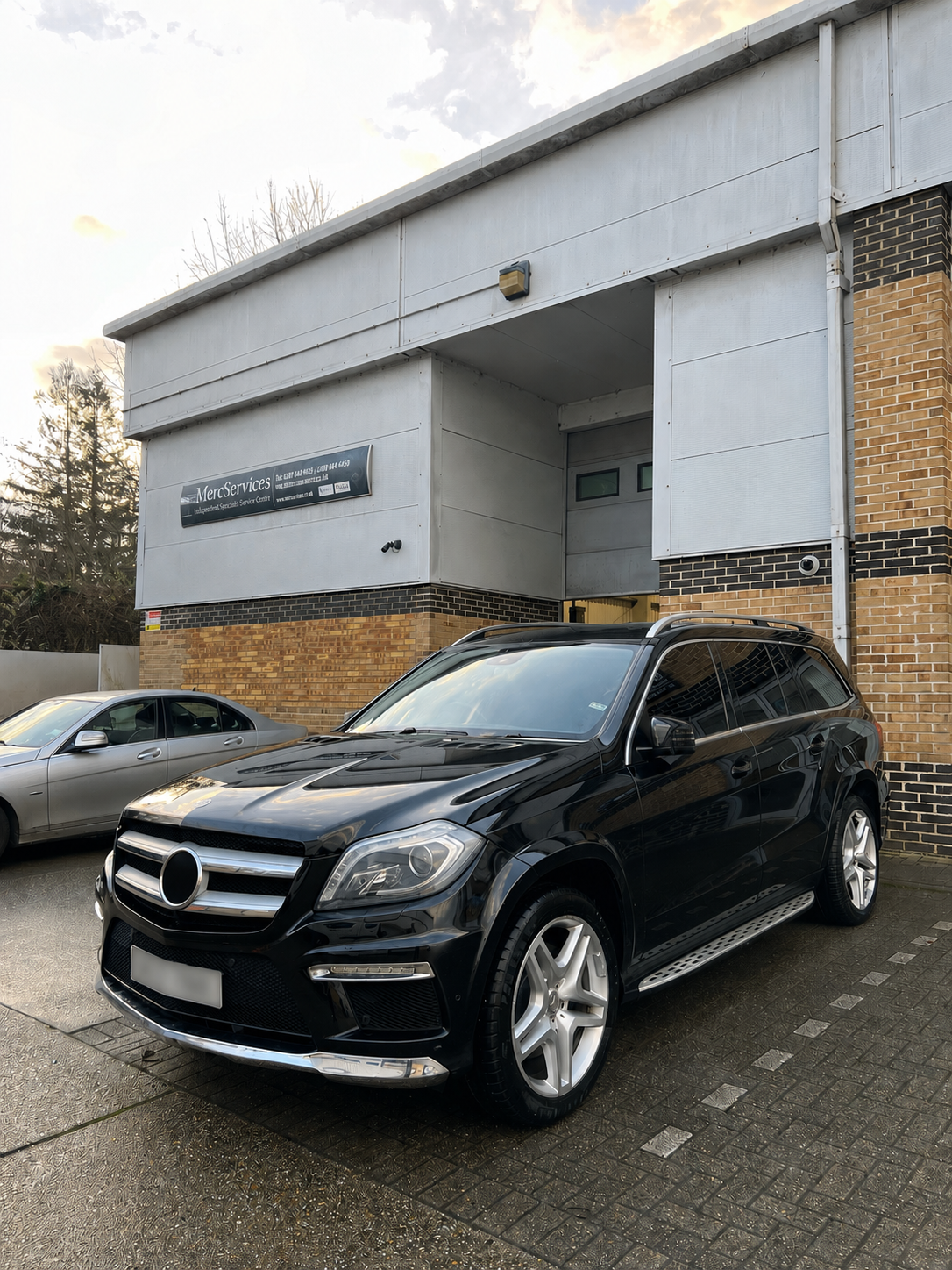 Black SUV parked in front of a modern brick and gray building, with another car parked beside it, during daytime.