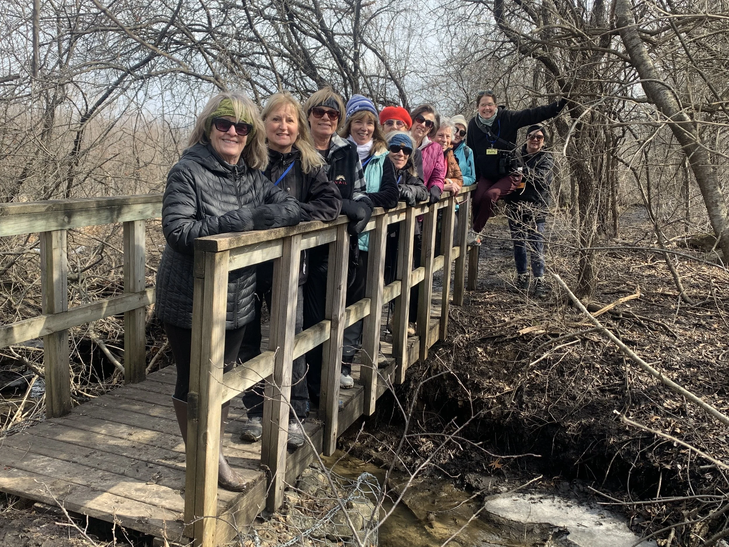 Group of women standing on a wooden bridge in a wooded area during winter.