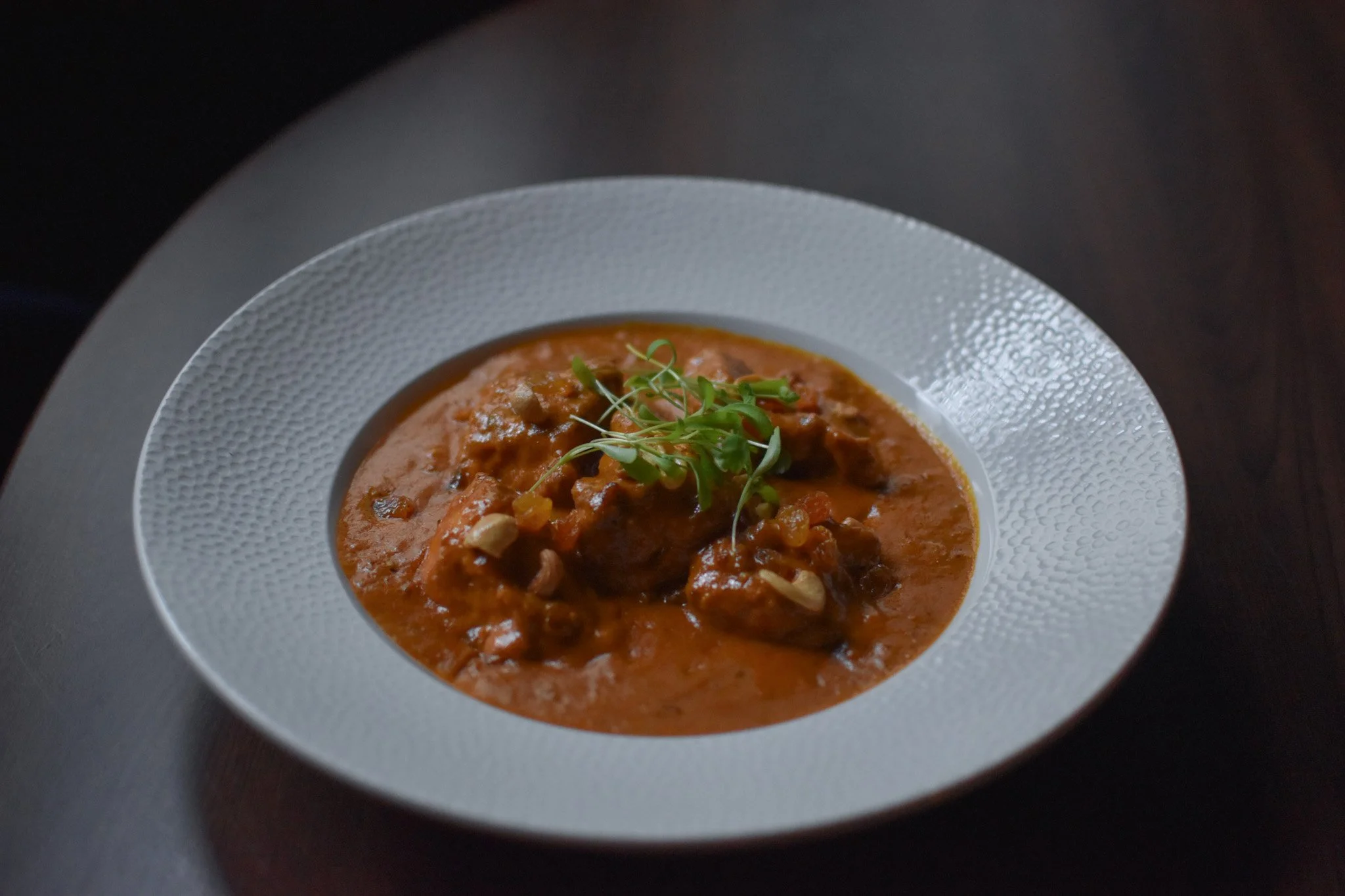 A white bowl with textured rim containing a serving of hearty beef stew garnished with microgreens.