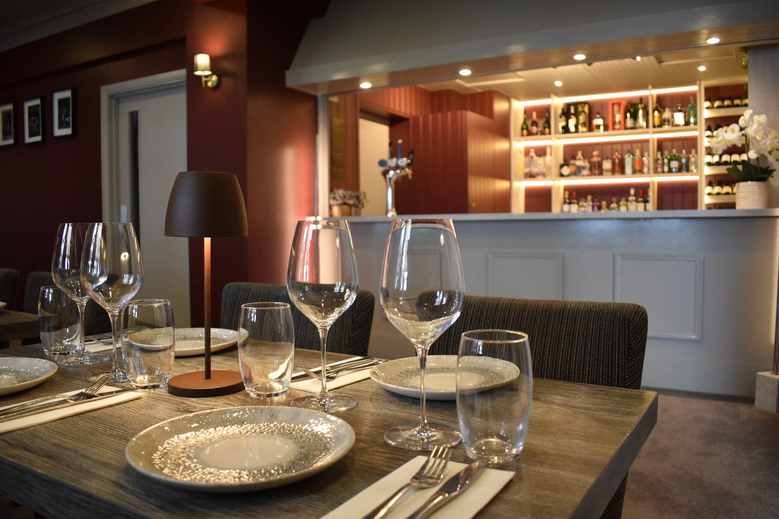 Elegant bar and dining area featuring a beautifully set table with wine glasses, with our fully stocked liquor bar in the background.