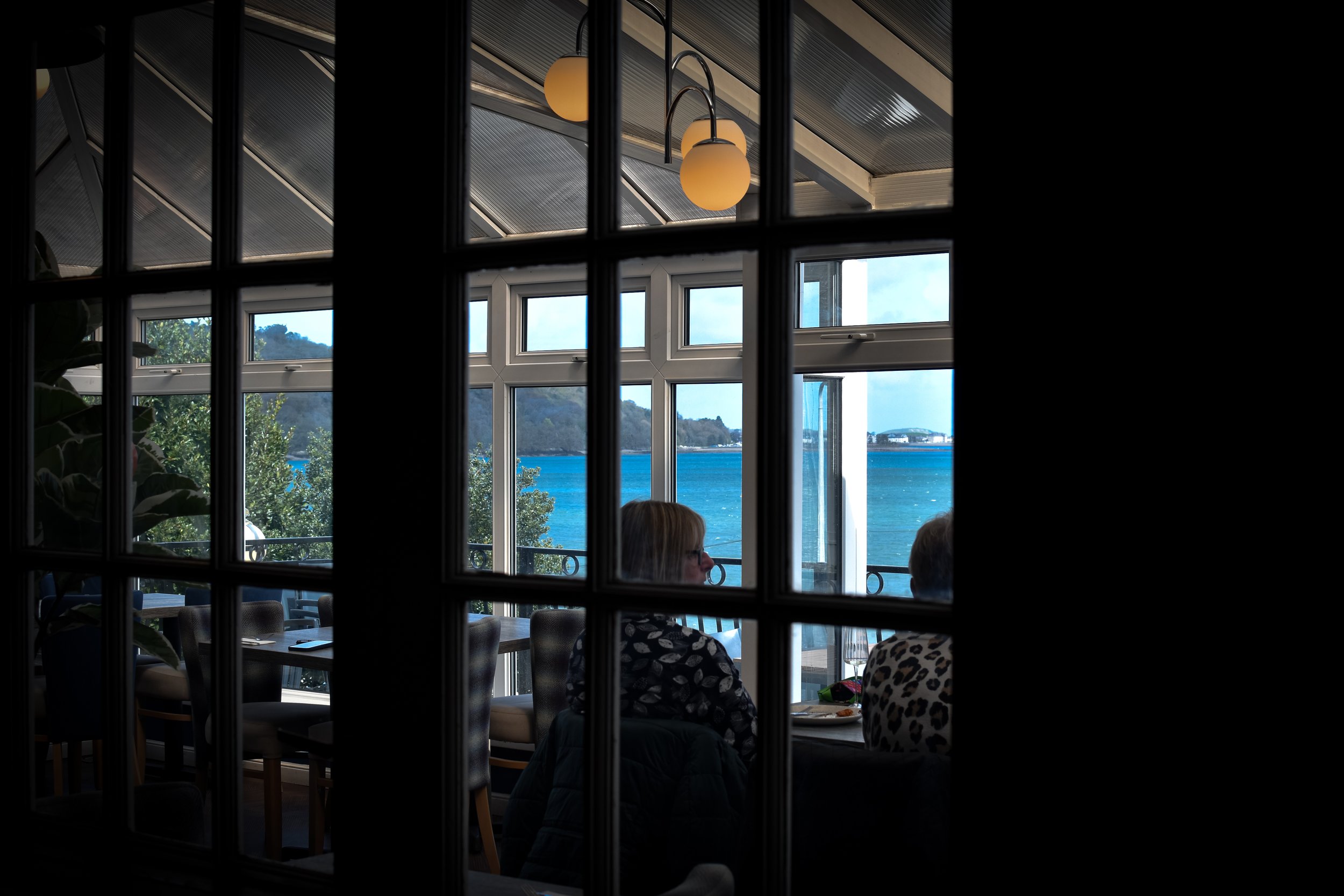 Diners enjoying a meal in our oceanfront conservatory restaurant, featuring large windows with stunning seaside and hillside views