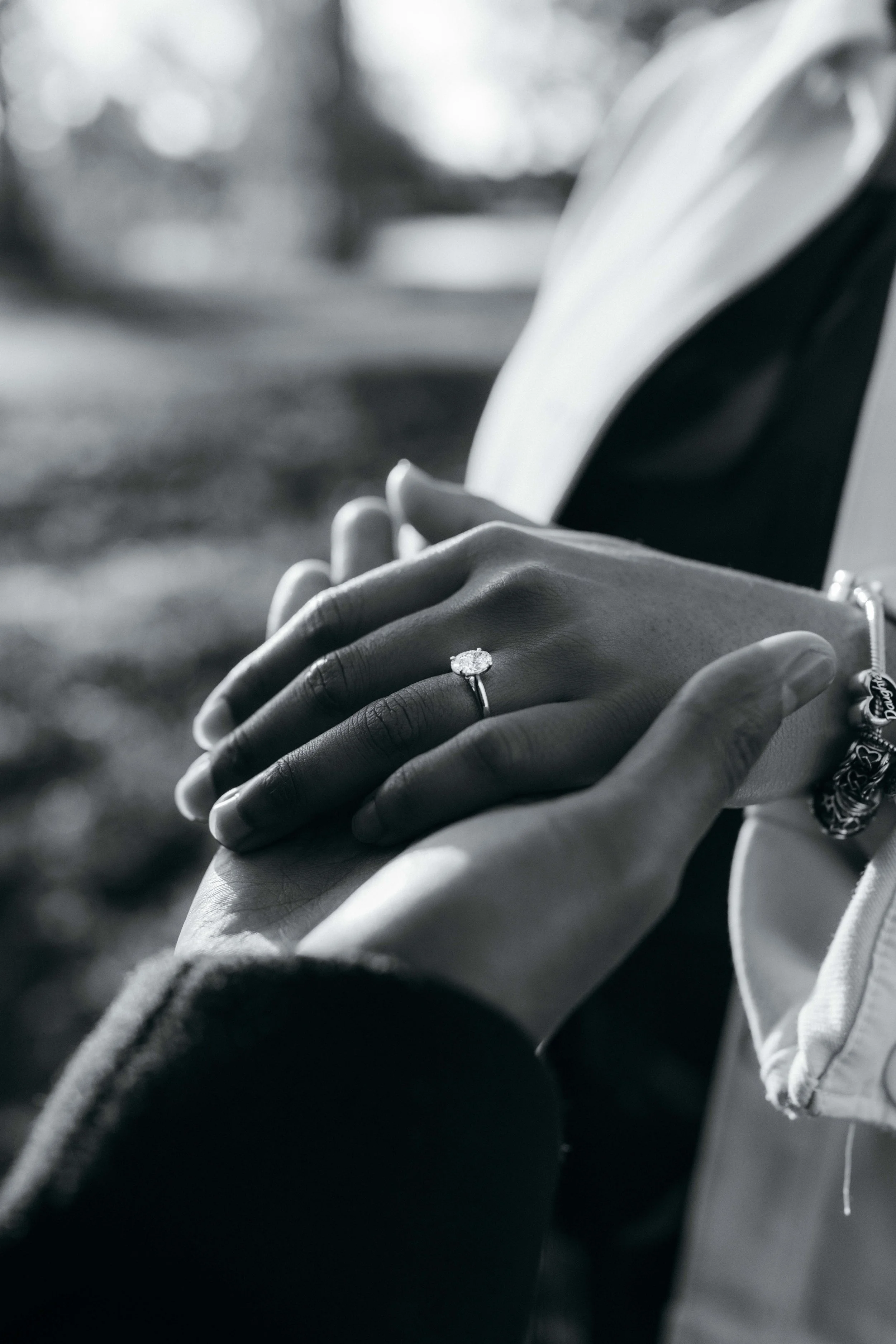 Close-up of two hands holding each other, with the woman wearing a ring on her finger, outdoors with blurred background.