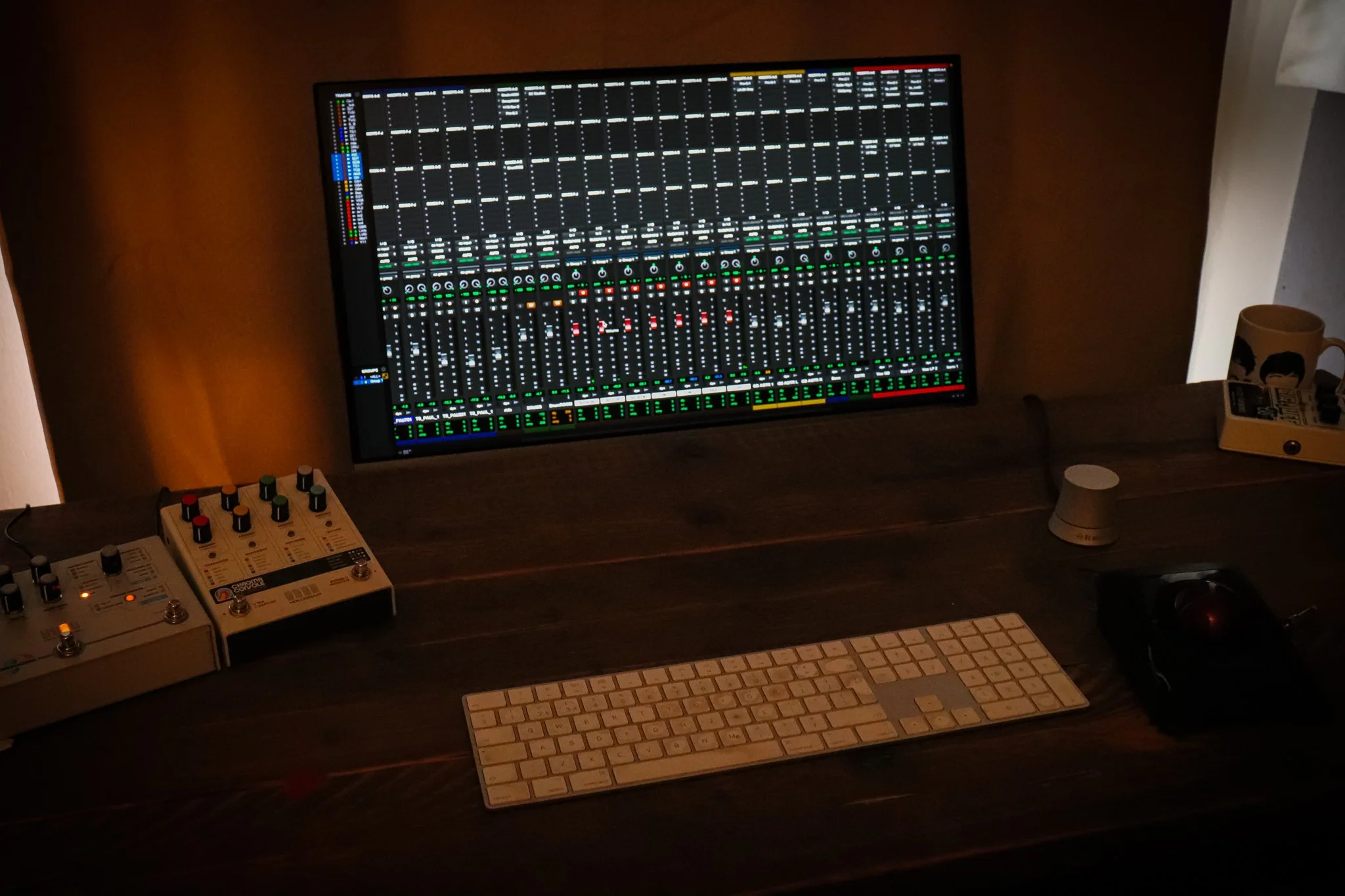 Music production setup featuring a large digital audio workstation on a desk with various audio equipment, a MIDI keyboard, and a computer keyboard.