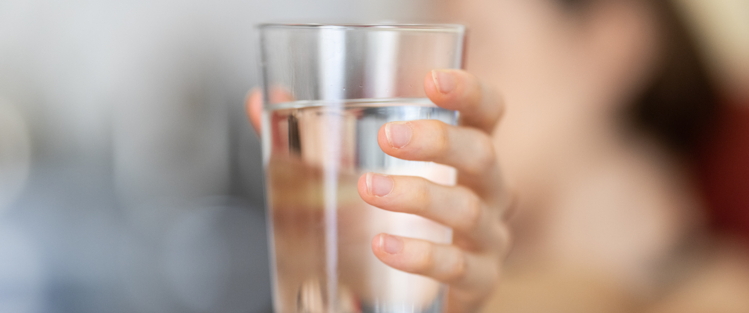 A hand holding a glass of water to stay hydrated during a summer heatwave.